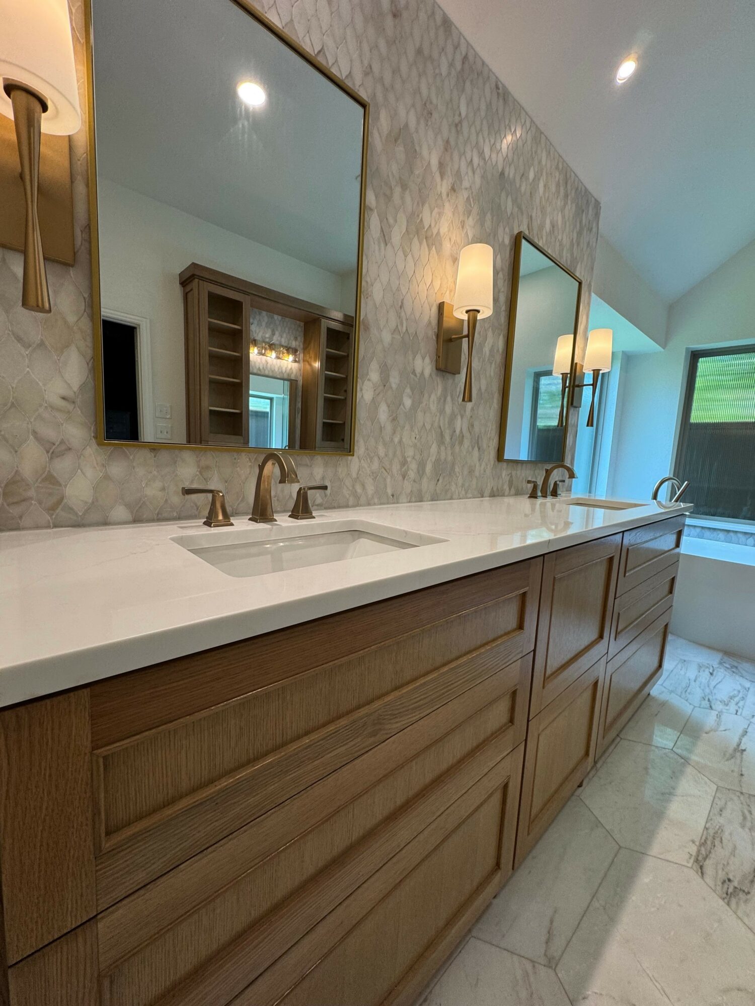 Bathroom vanity with two mirrors, a marble countertop, and wooden cabinets, with a window and marble floor.
