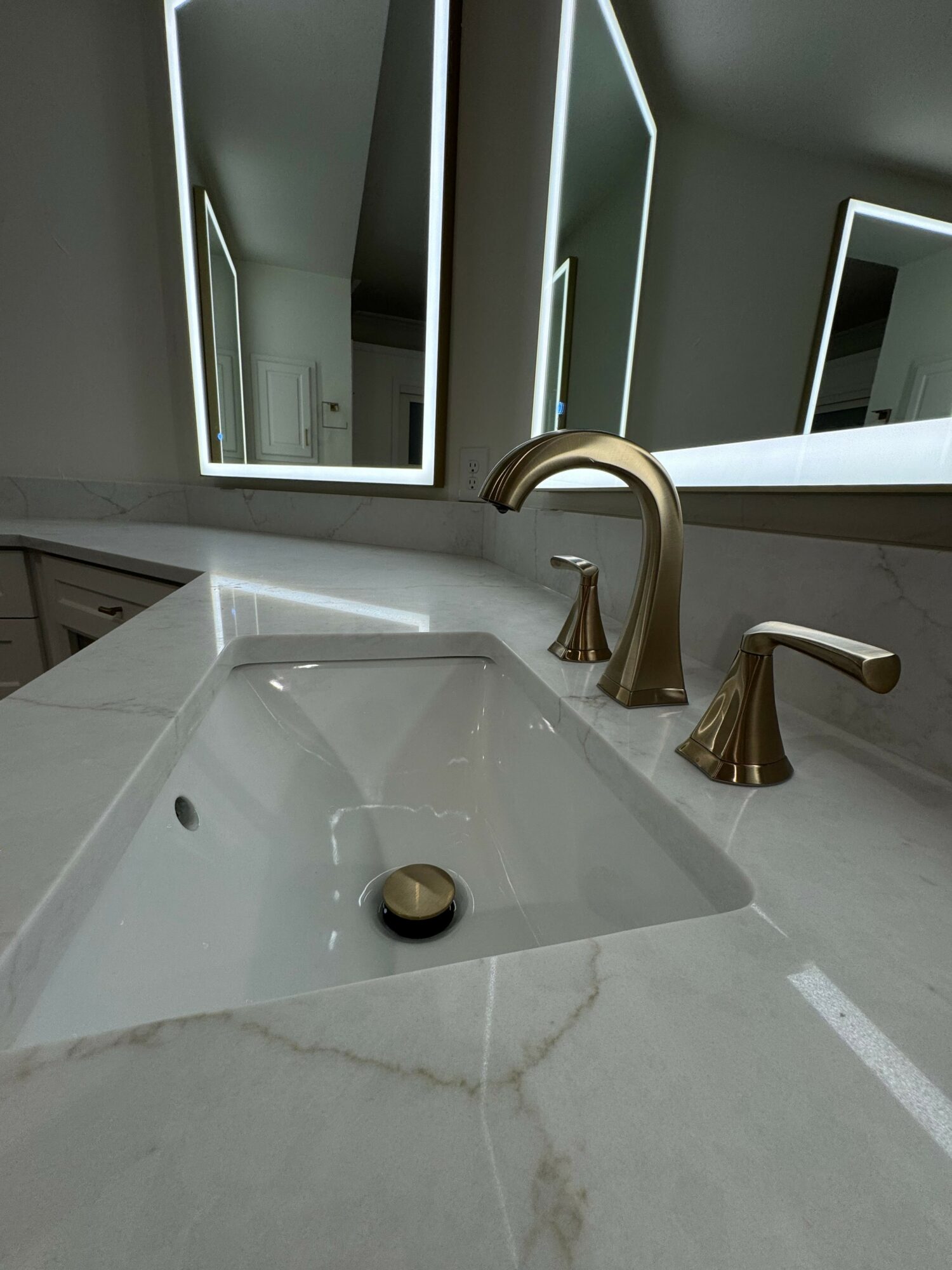 Bathroom sink with gold faucet and mirror, viewed from above, with a window in the background.