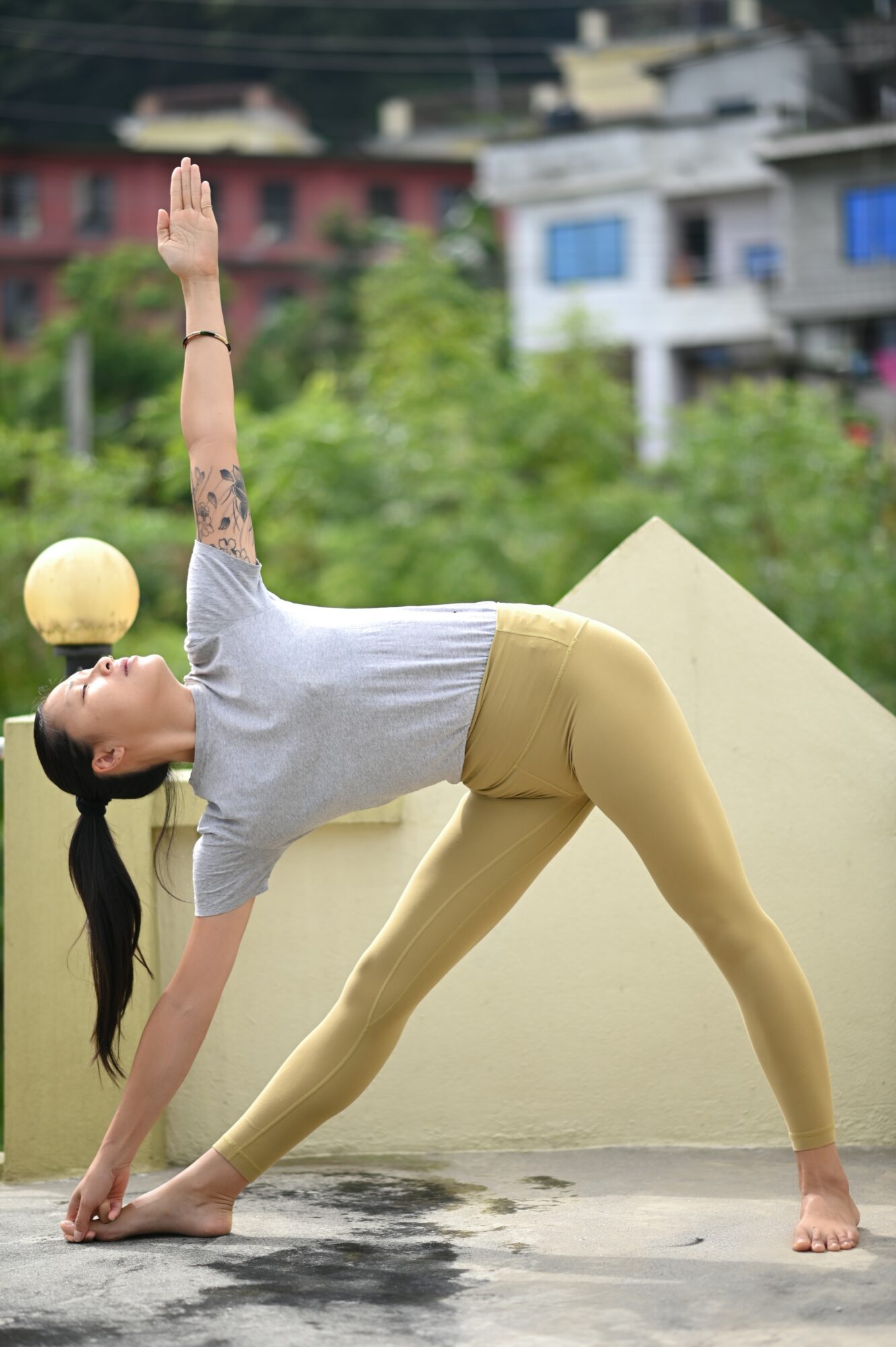 Woman practicing yoga outdoors on a rooftop, in a side stretch pose with one arm raised and the other touching the ground.