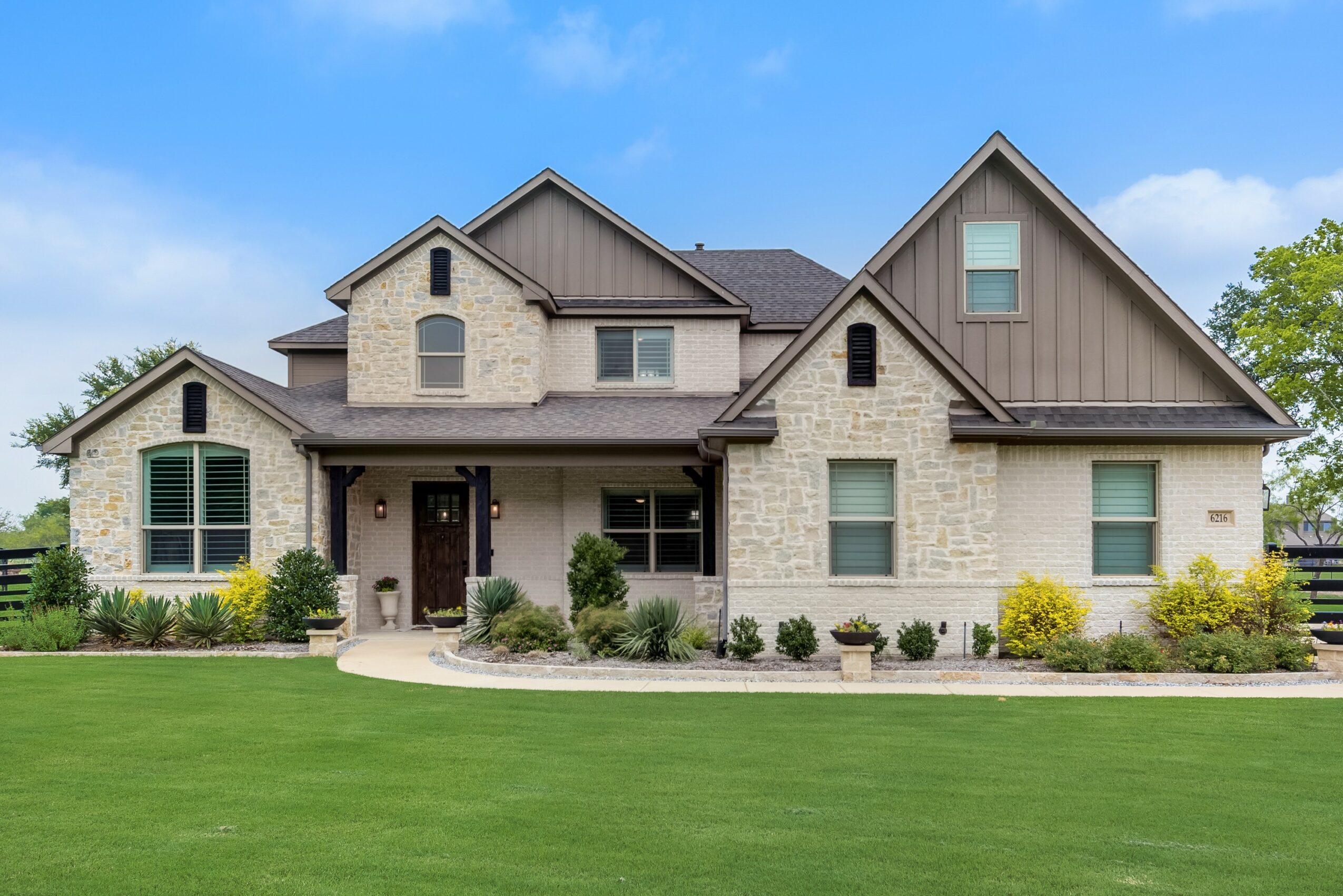 Large house with brick and wood exterior, multiple gabled roofs, front porch, and well-maintained lawn with shrubs.