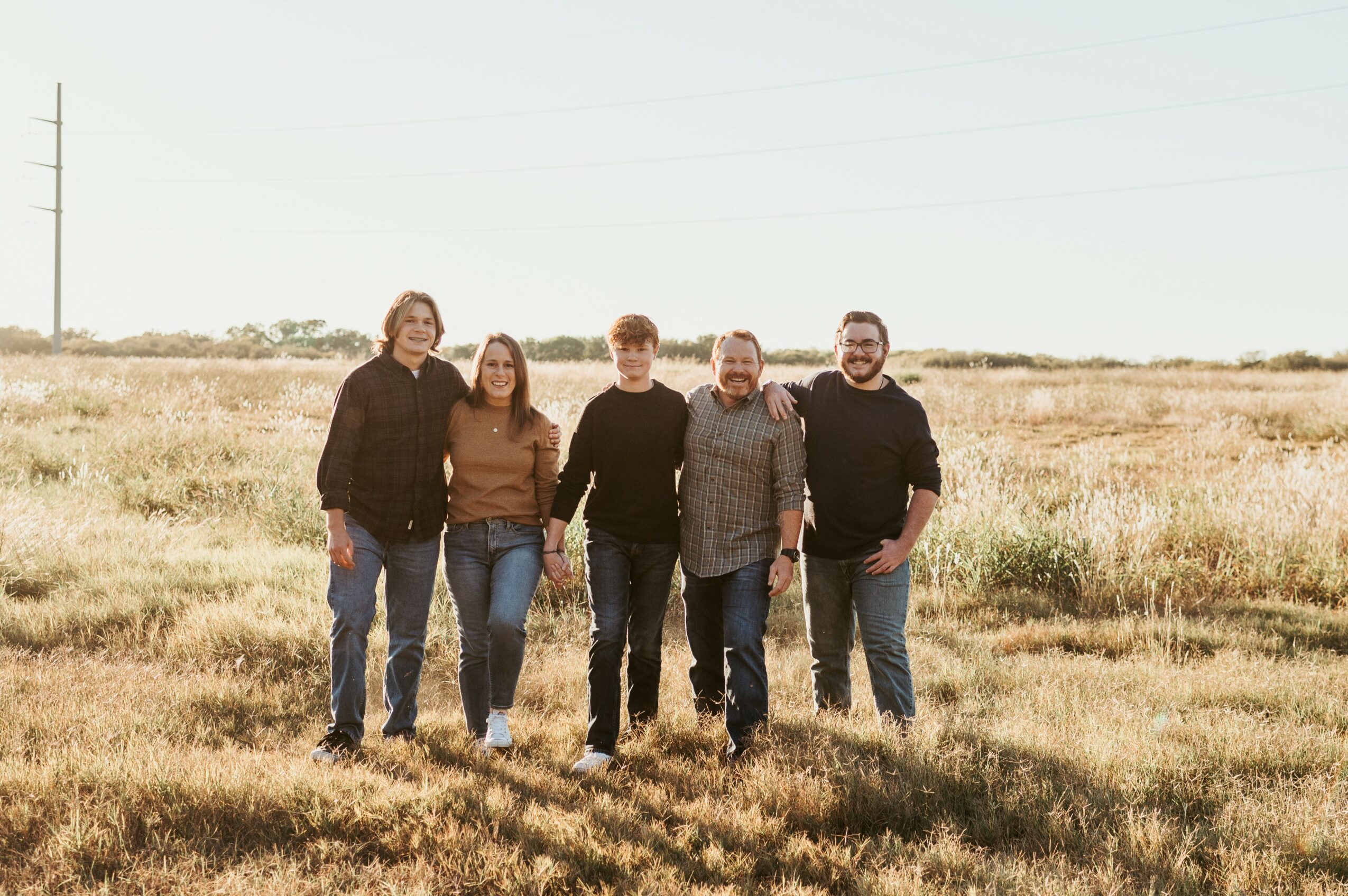 Five people walking together in a field, holding hands, with a clear sky and open landscape behind them.