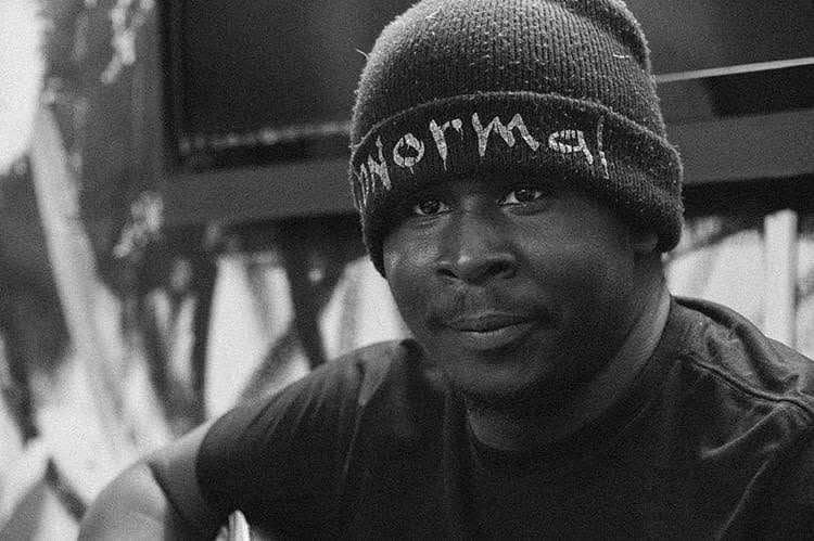 Man wearing a beanie hat with text, looking at the camera, in black and white.