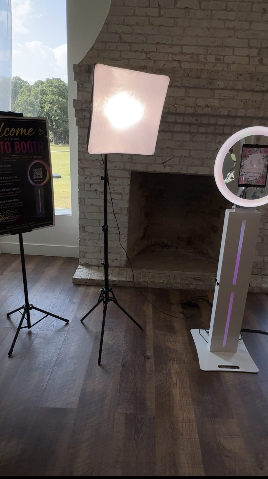 Photo of a photography setup with a softbox light, ring light, and a signboard indoors near a brick fireplace.