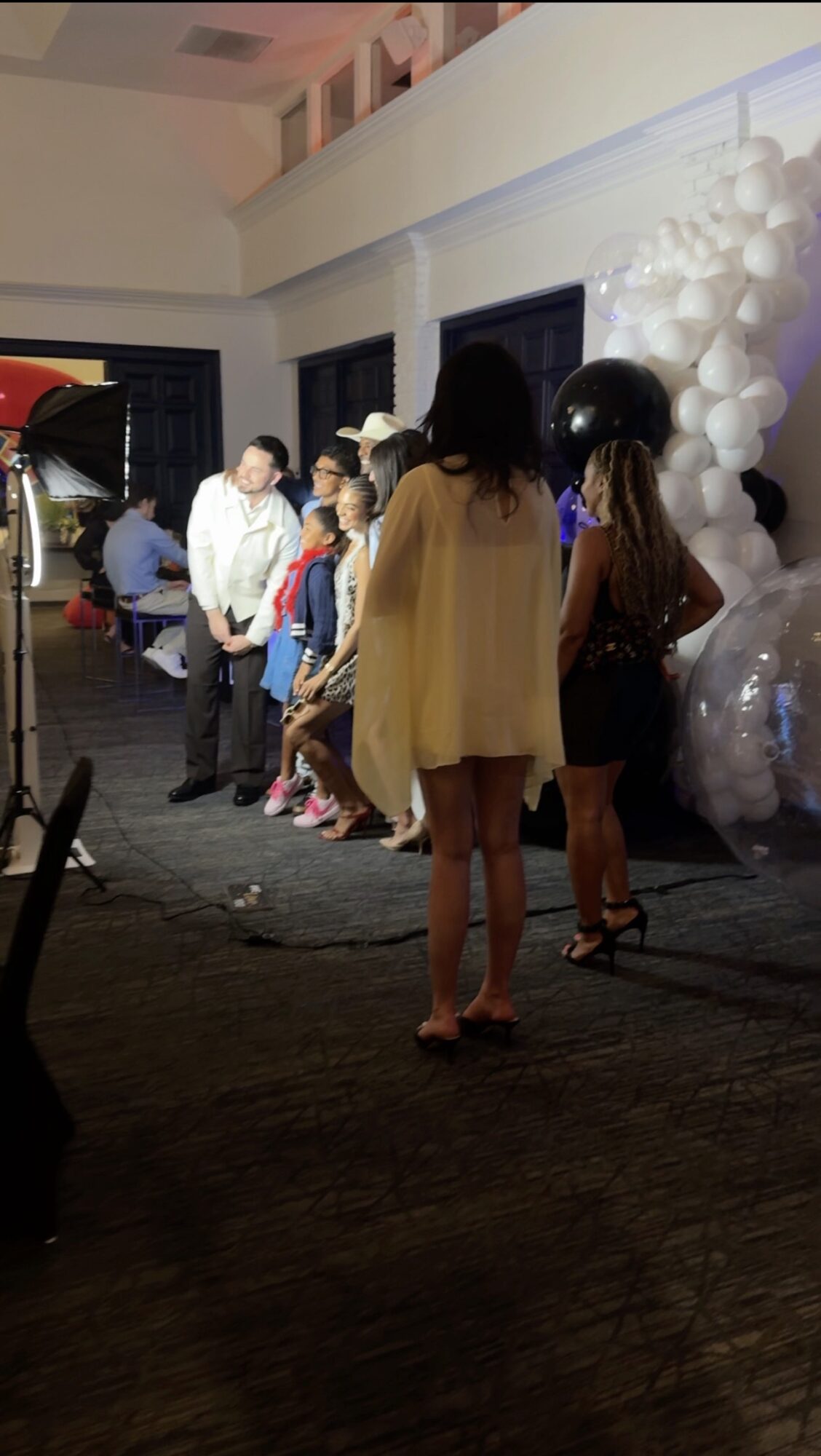 People standing in line indoors near white balloon decorations, some facing away from the camera.