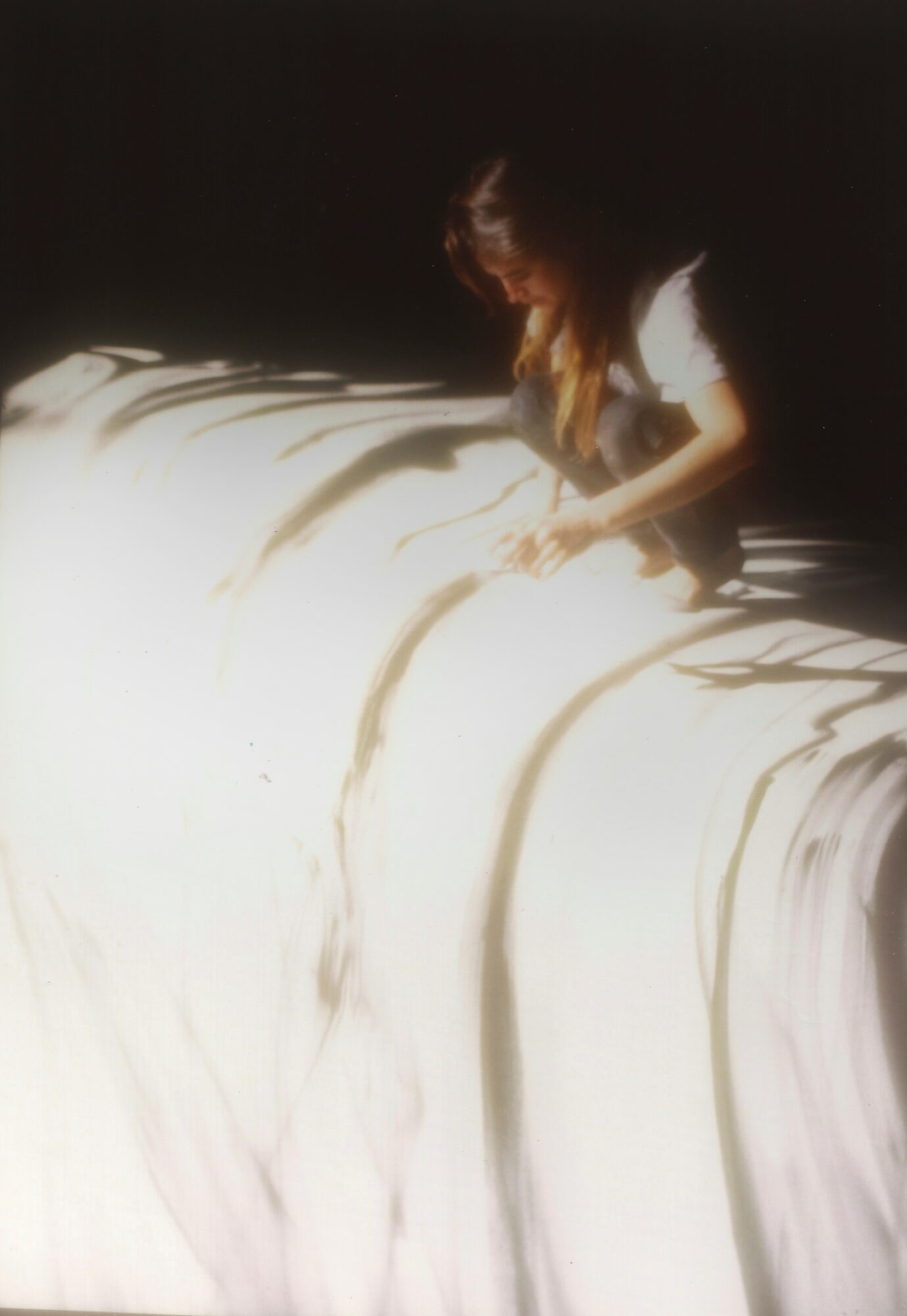 Person with red hair leaning over a large, flowing white surface, possibly a waterfall or fabric, in a dark environment.