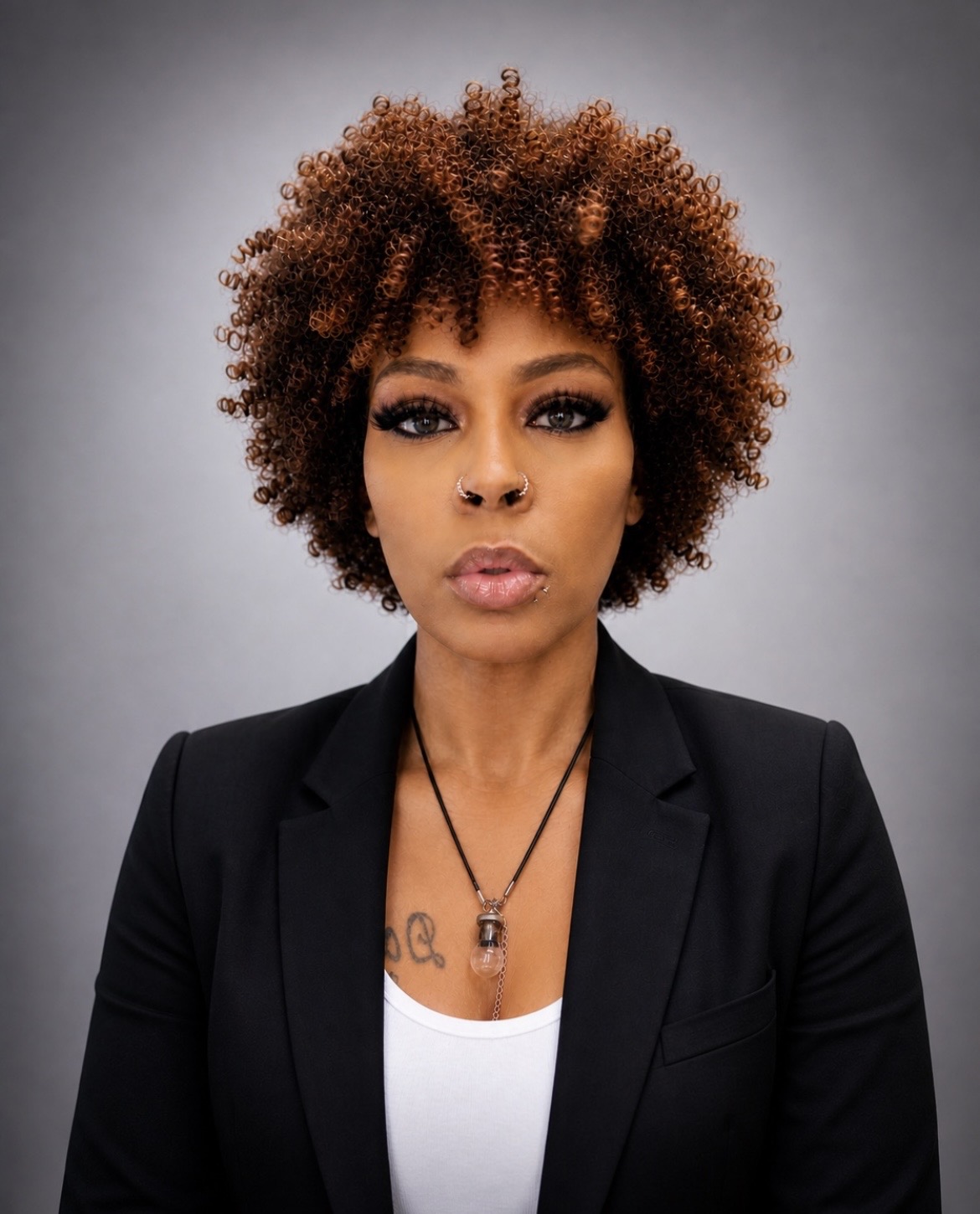 Woman with curly hair wearing a black blazer and white top, looking directly at the camera.