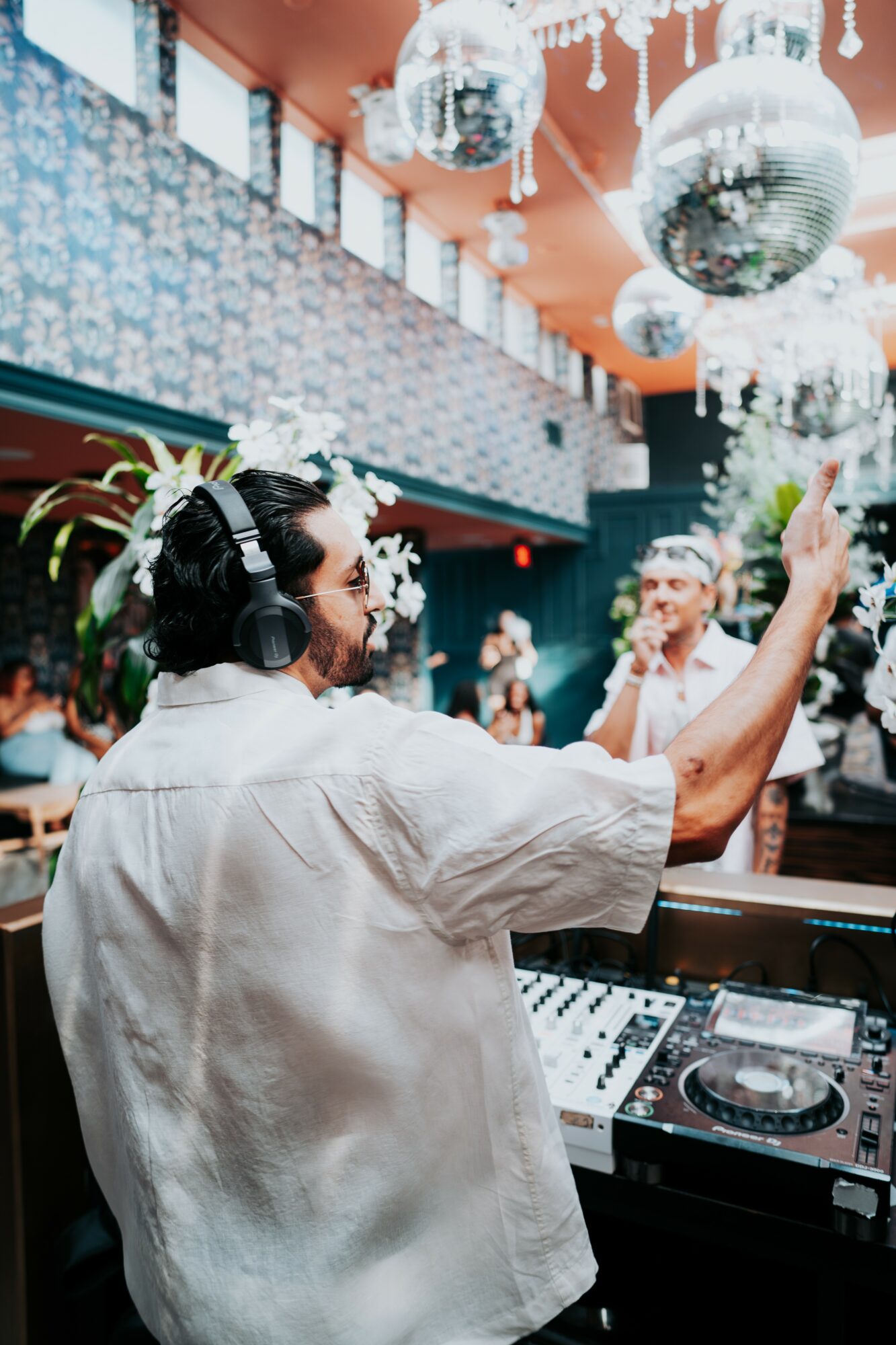 Person with headphones and a white shirt dancing at a party with disco balls overhead.