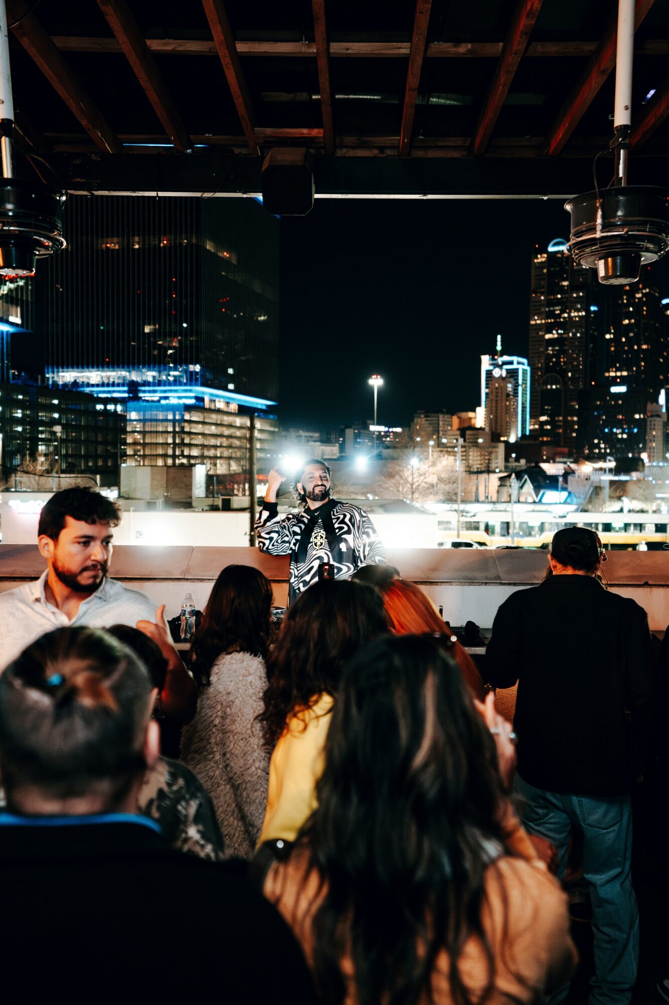 People gathered outdoors at night with city buildings and lights in the background.