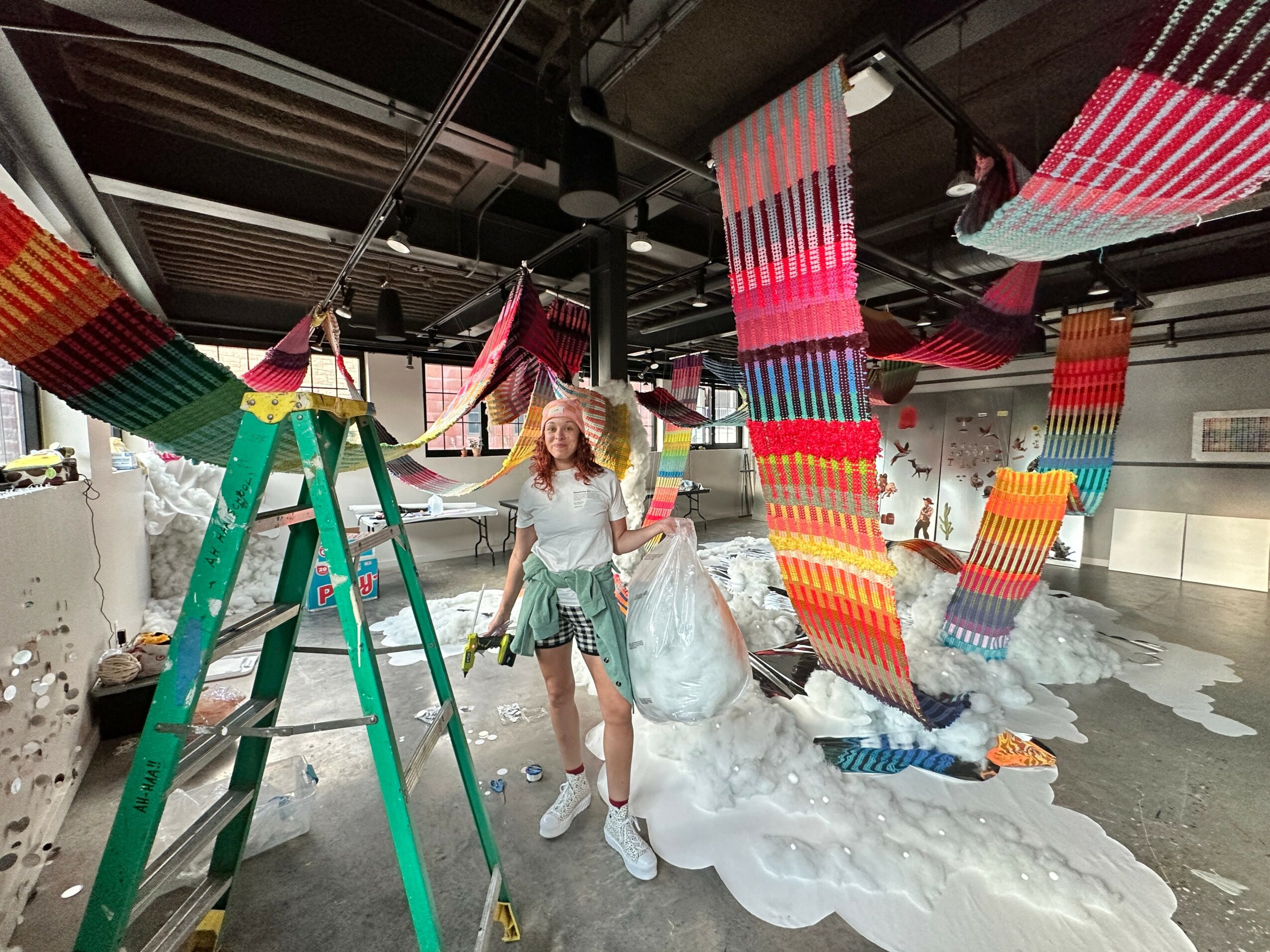 Person standing in an art installation with colorful hanging fabric and foam on the floor.