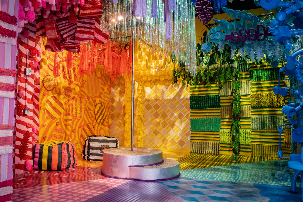 Colorful, decorated room with wrapped presents, a small platform, and hanging decorations in vibrant colors.