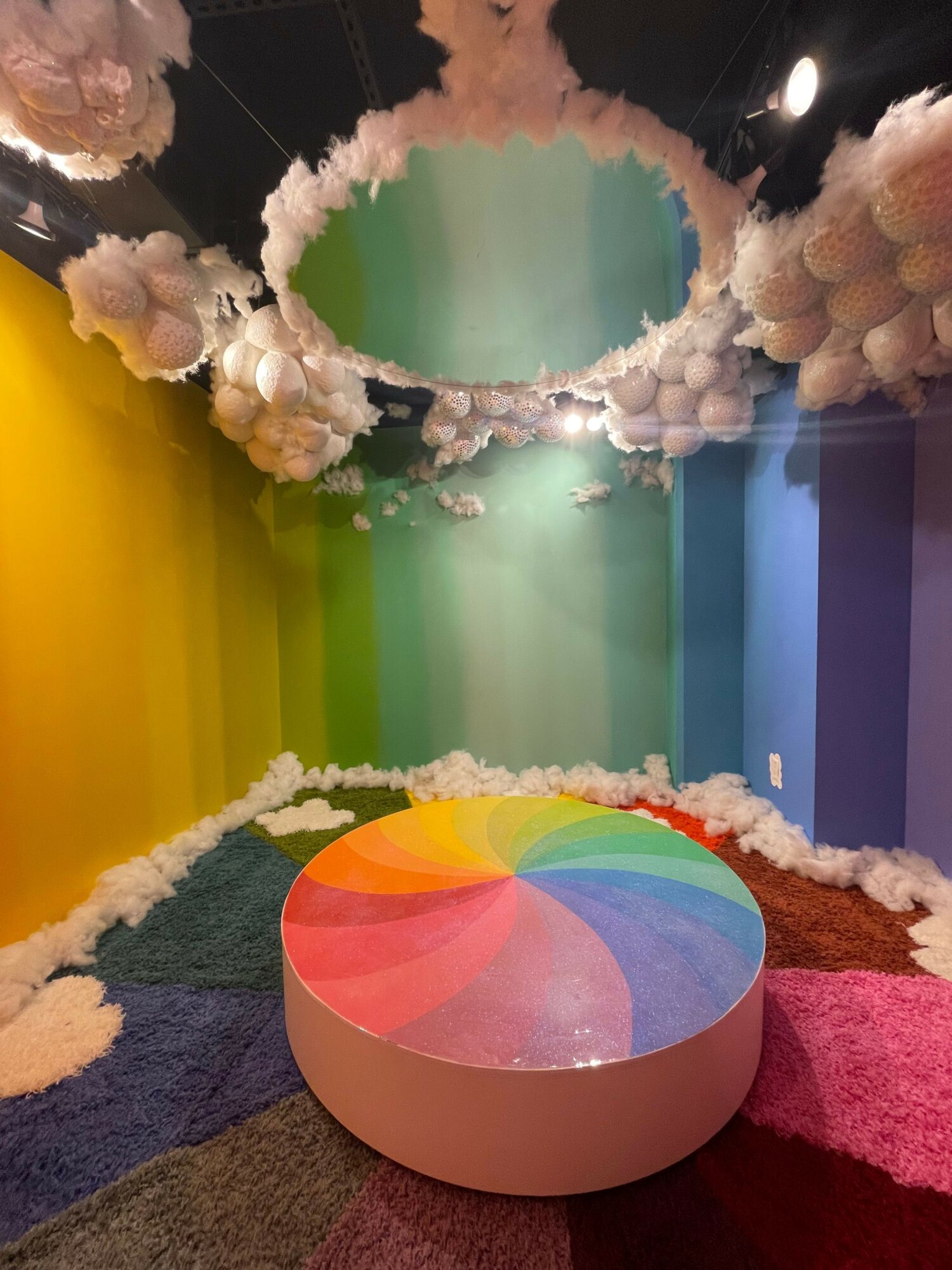 Colorful circular platform with rainbow segments, surrounded by cloud-like decorations, in a vibrant, multicolored setting.