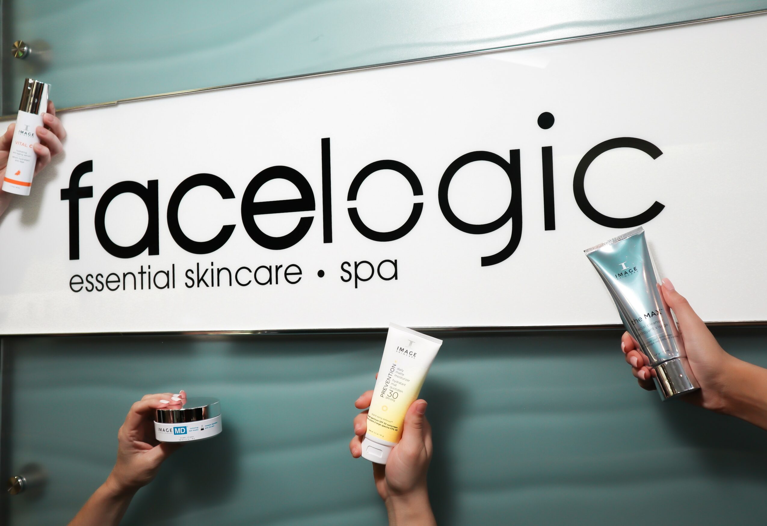 People hold skincare products in front of a sign reading 'facelogic essential skincare spa'.