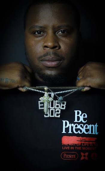 Close-up of a person holding necklaces, wearing a black shirt with text, in a dark background.