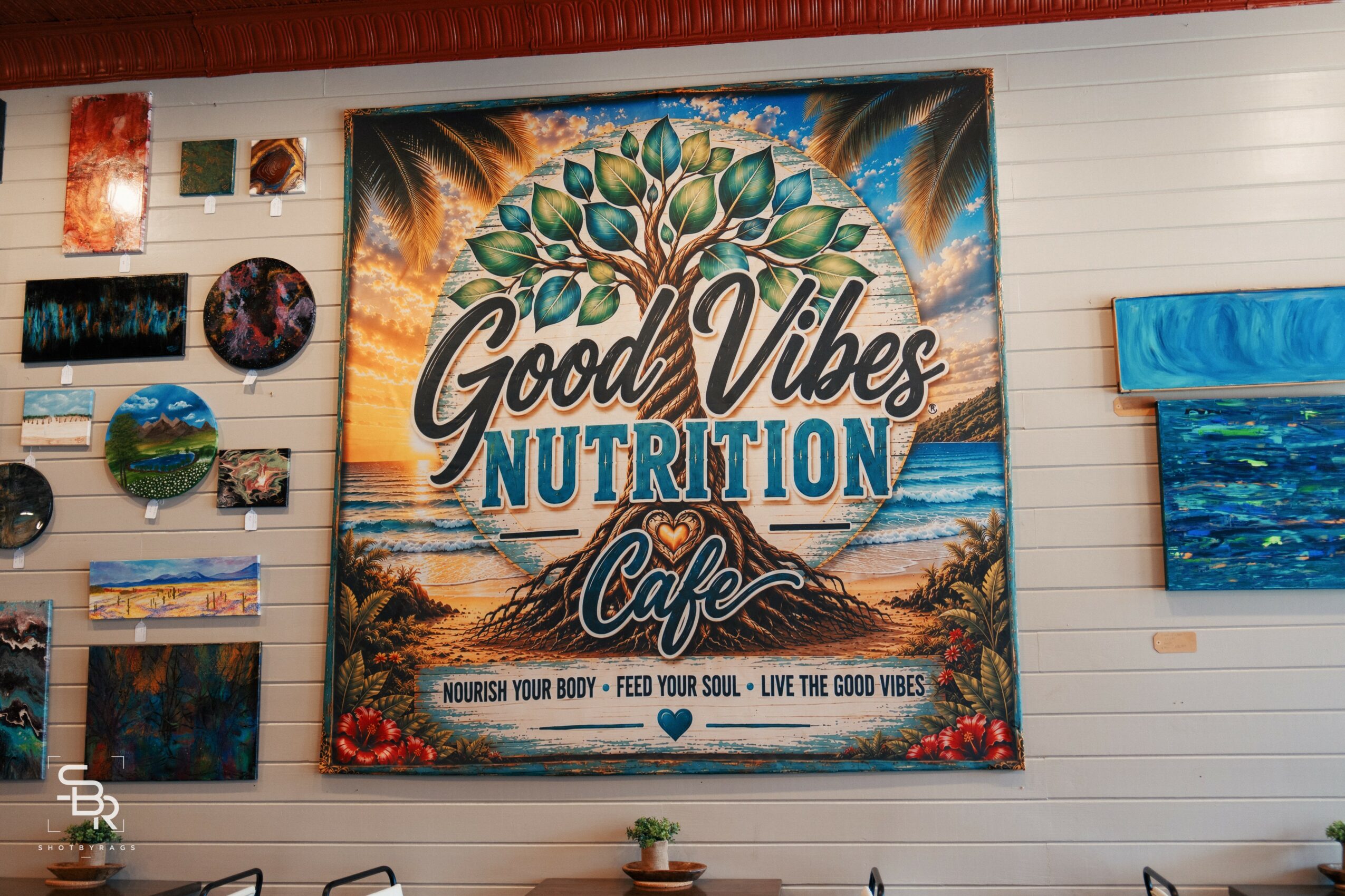 Sign for Good Vibes Nutrition Cafe with a tree and sunset background, promoting health and positive energy.