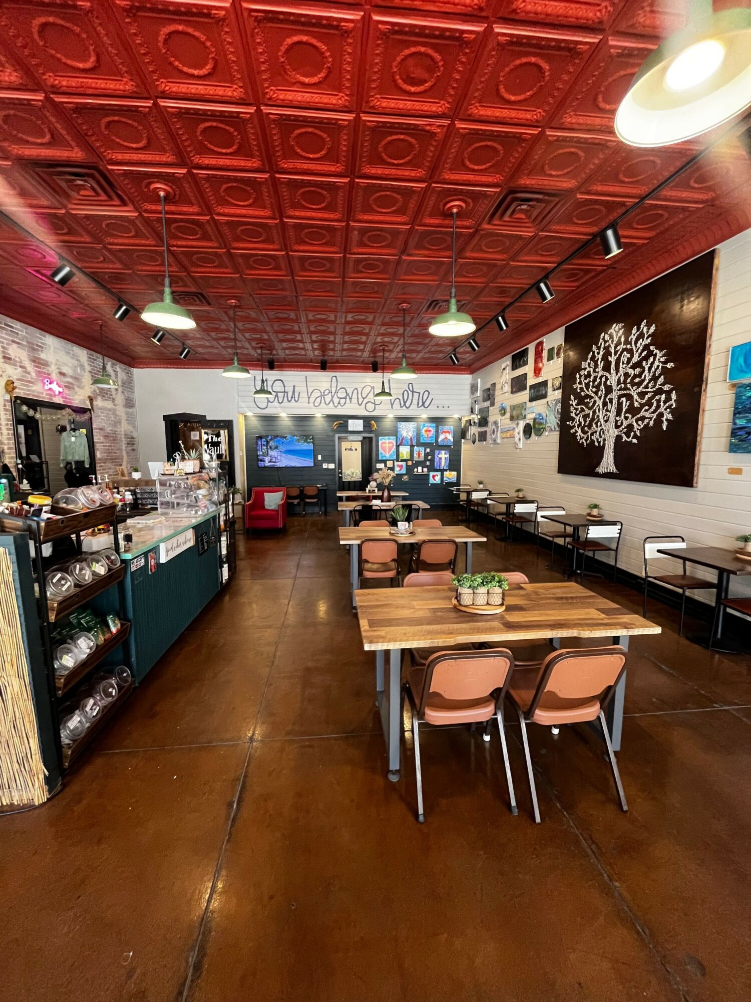 Interior of a cafe with a red patterned ceiling, wooden floor, tables, chairs, and a counter with various items.