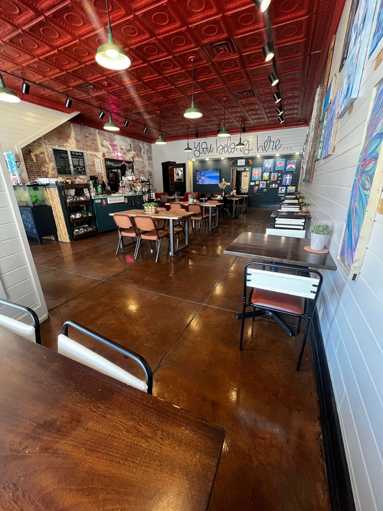 Room with a wooden floor, tables, chairs, and a bar area with various bottles and equipment, viewed from the side.