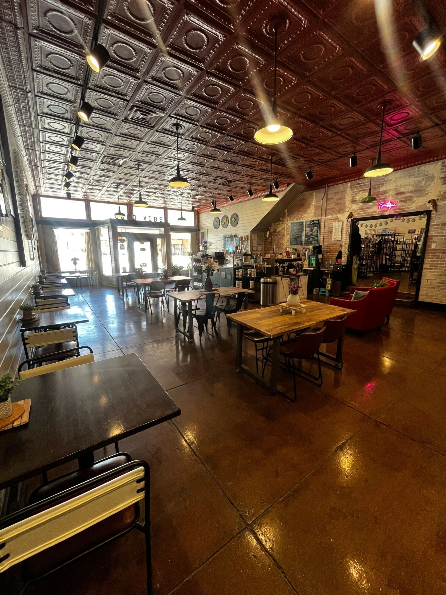 Interior of a restaurant with tables, chairs, and a patterned ceiling, illuminated by warm lighting, with a view toward the entrance.
