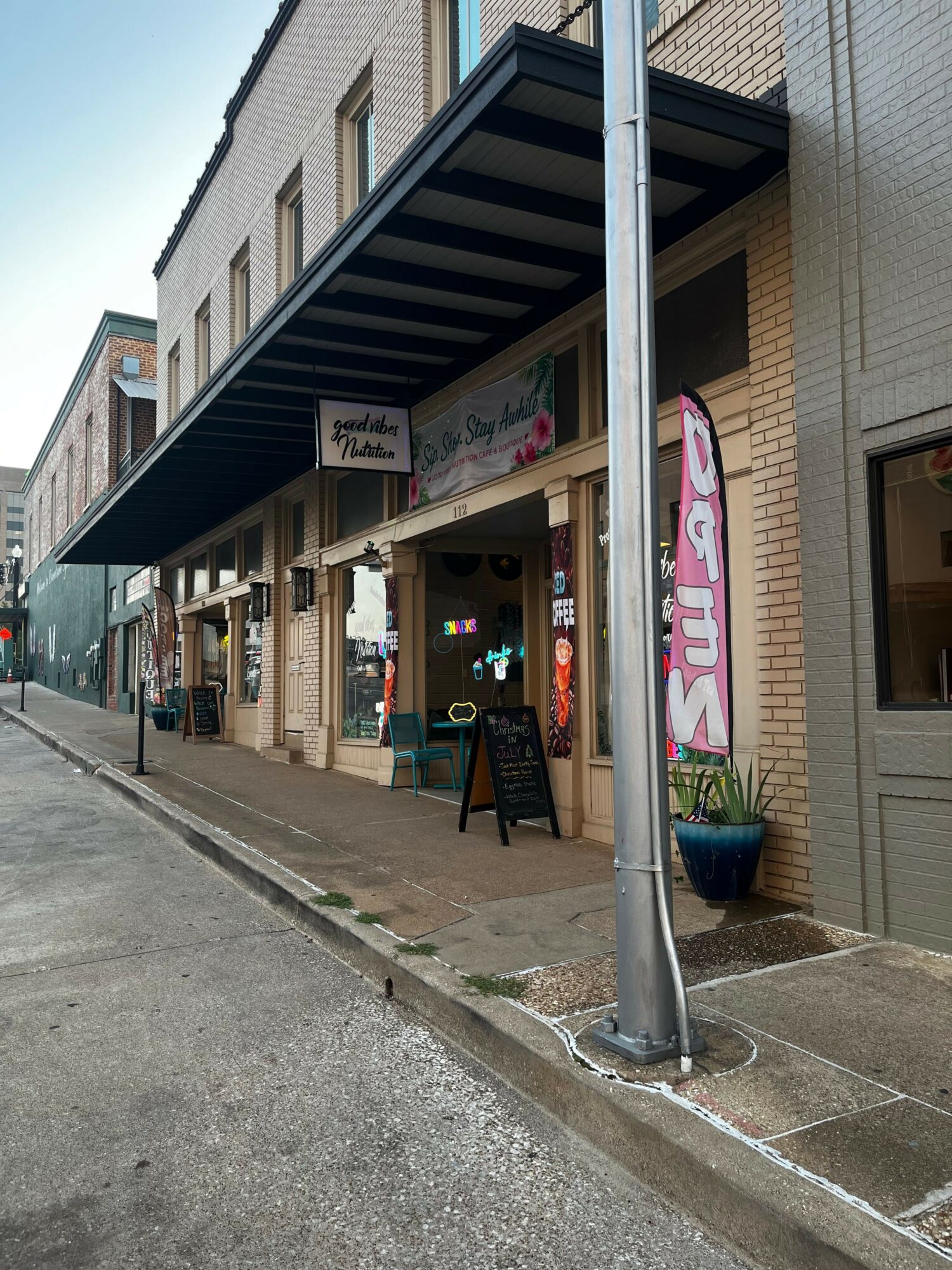 Store entrance with a black awning, glass door, and sidewalk outside, with a pole in front.