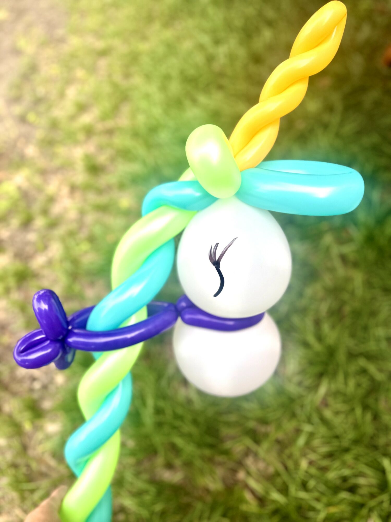 Colorful balloon unicorn with a twisted horn and mane, floating against a grassy background.