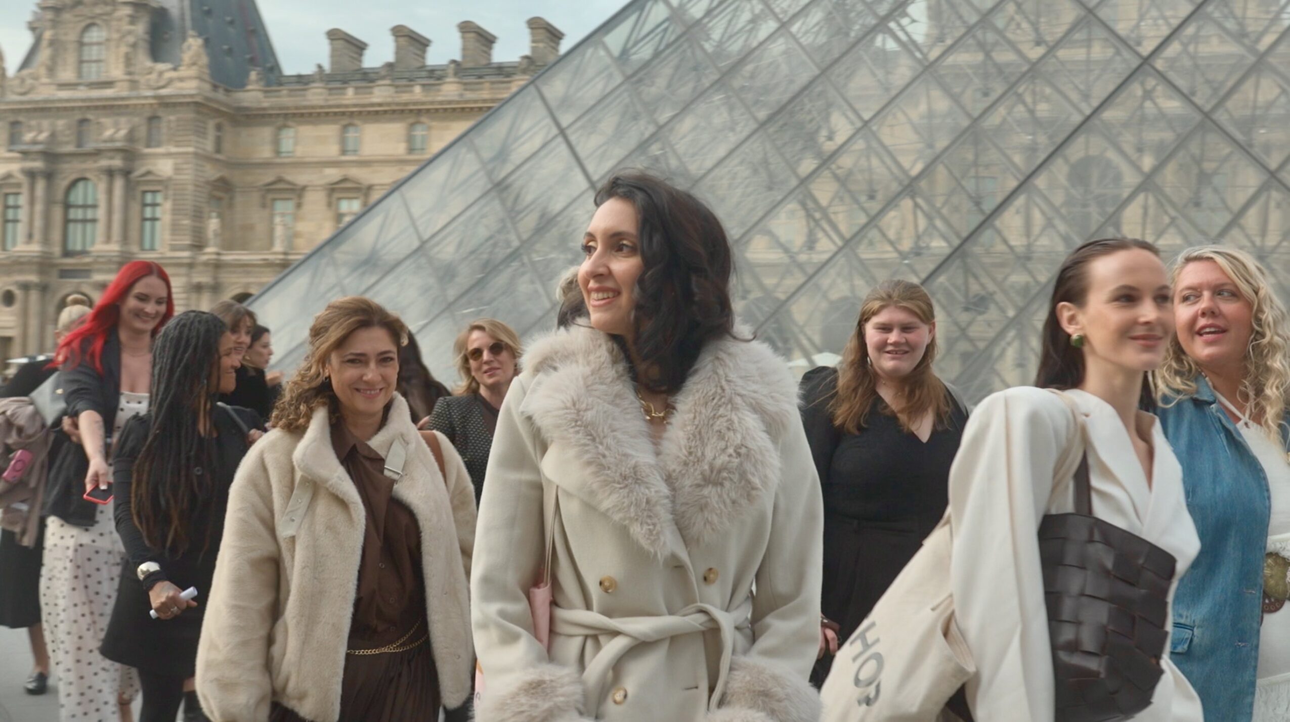 Group of women walking outdoors near a glass building, smiling and talking, with historic architecture in the background.