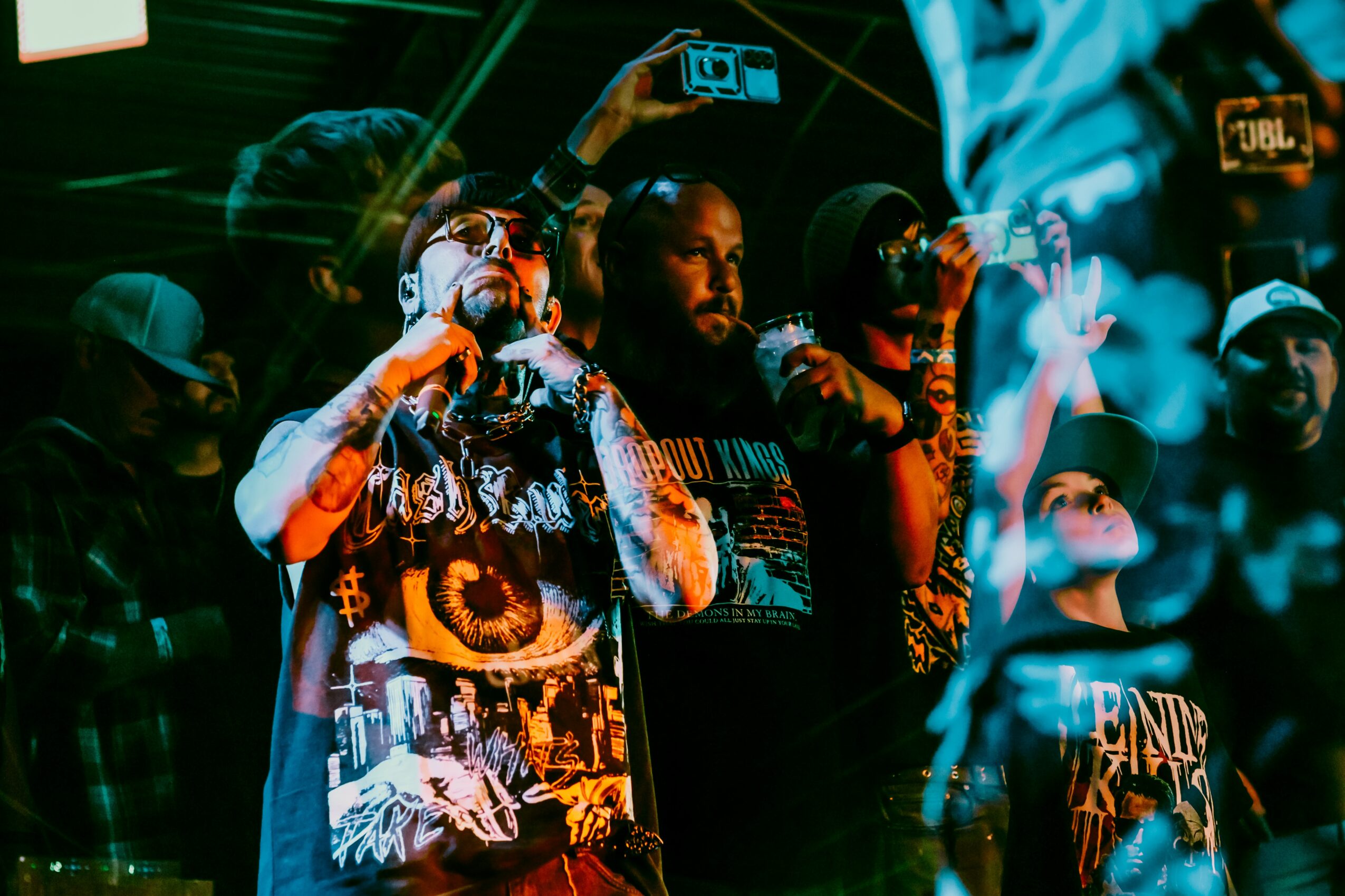 Group of people performing on stage with microphones, colorful lighting, and a crowd in the background.