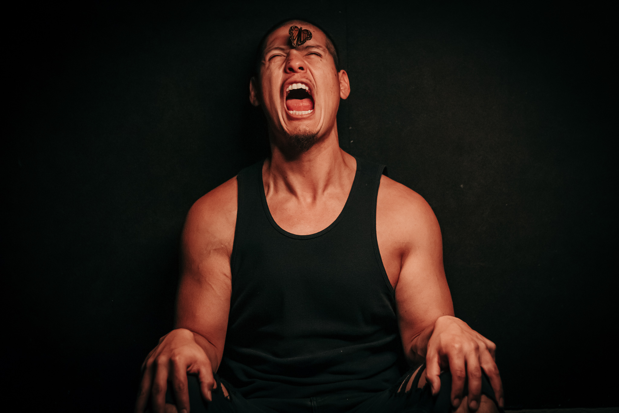 Person with short hair and a black tank top appears to be shouting or crying, with hands clenched and eyes closed.