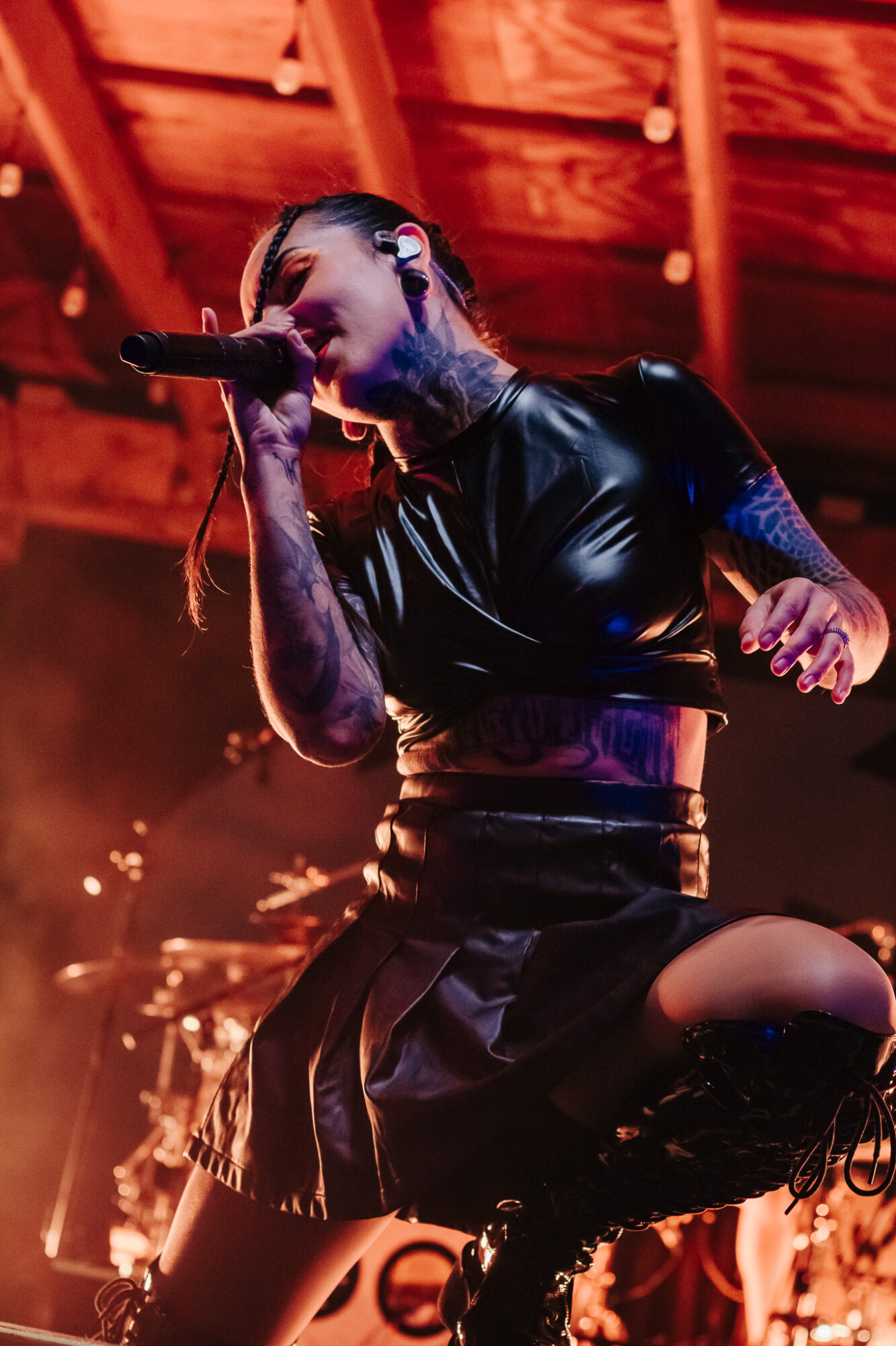 Female singer performing on stage with microphone, wearing black outfit, under warm stage lighting.