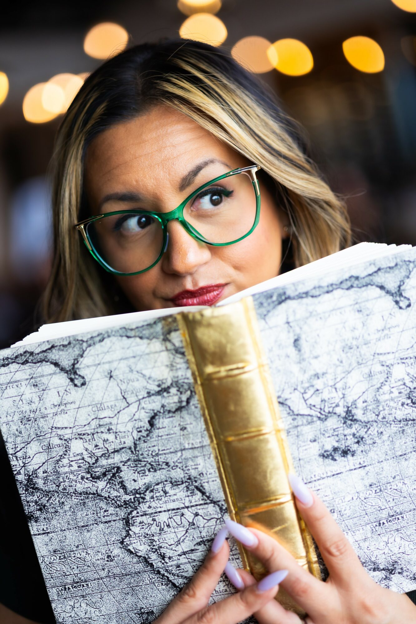 Woman with glasses reading a large map, with blurred lights in the background.