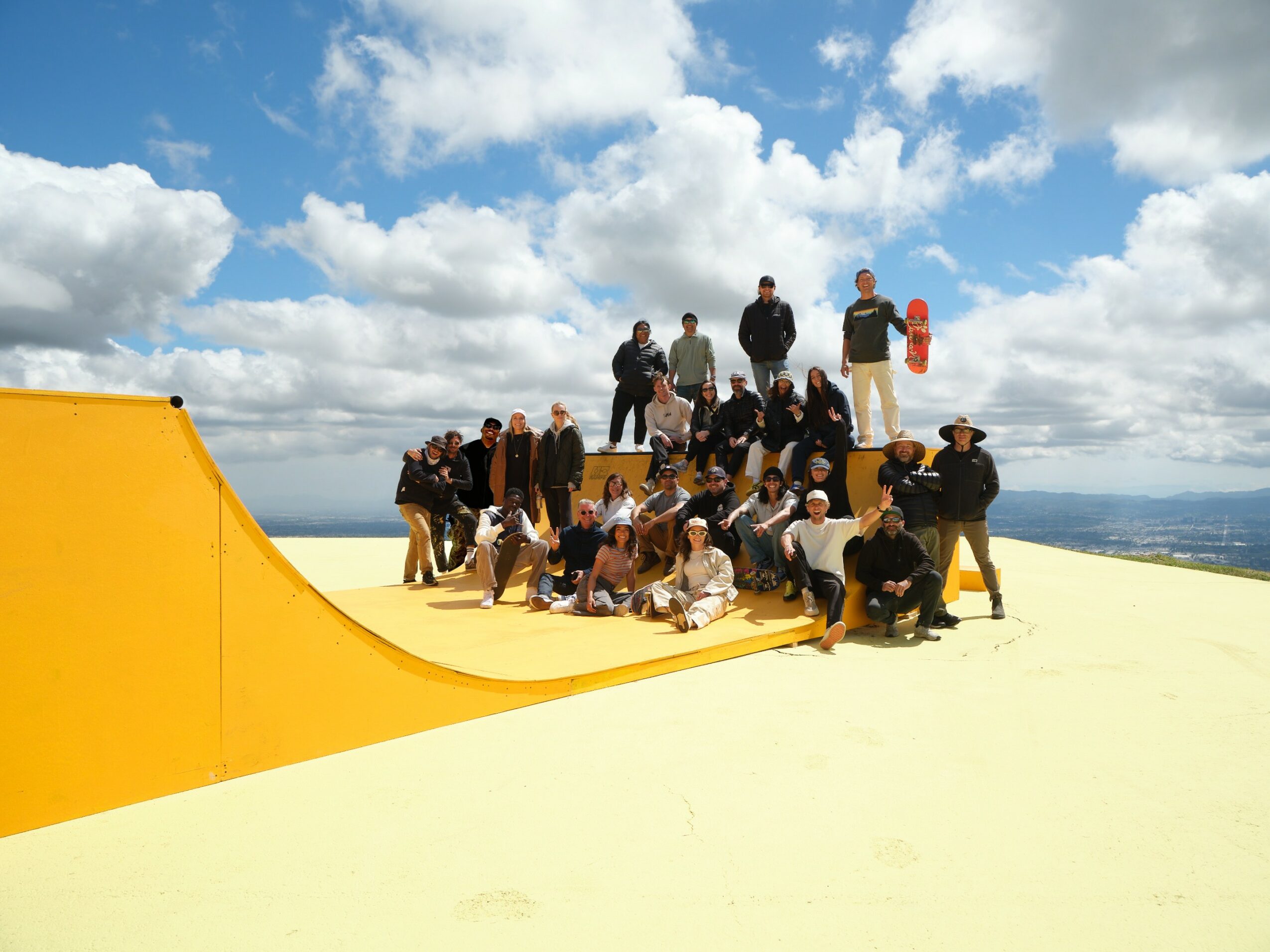 Group of people on a yellow skate park ramp outdoors under a blue sky with clouds.