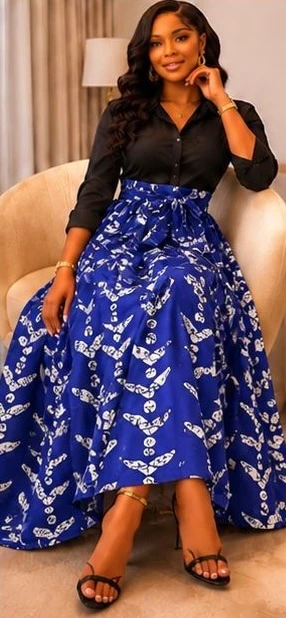 Woman in black top and blue patterned skirt sitting on a sofa, smiling, with a beige curtain in background.