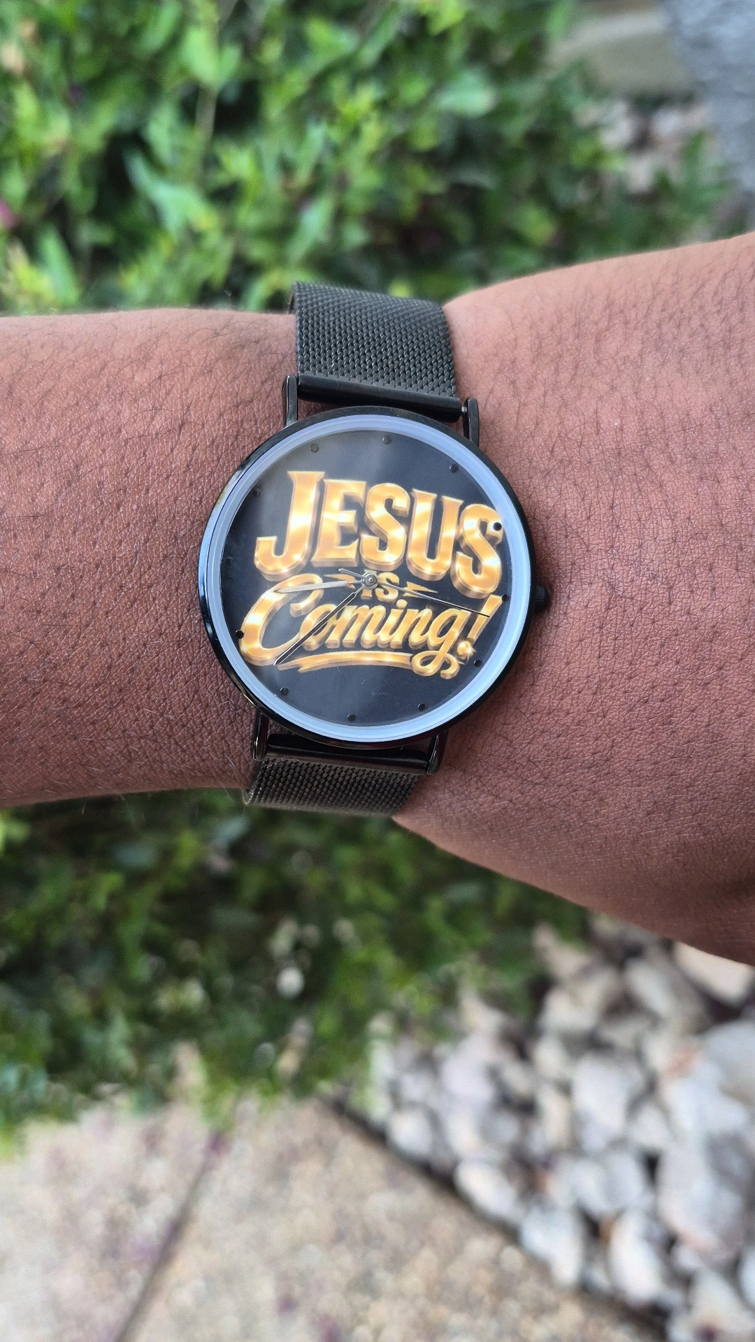 Person's wrist wearing a watch with a round face displaying the text 'JESUS Coming!' in gold and white letters.
