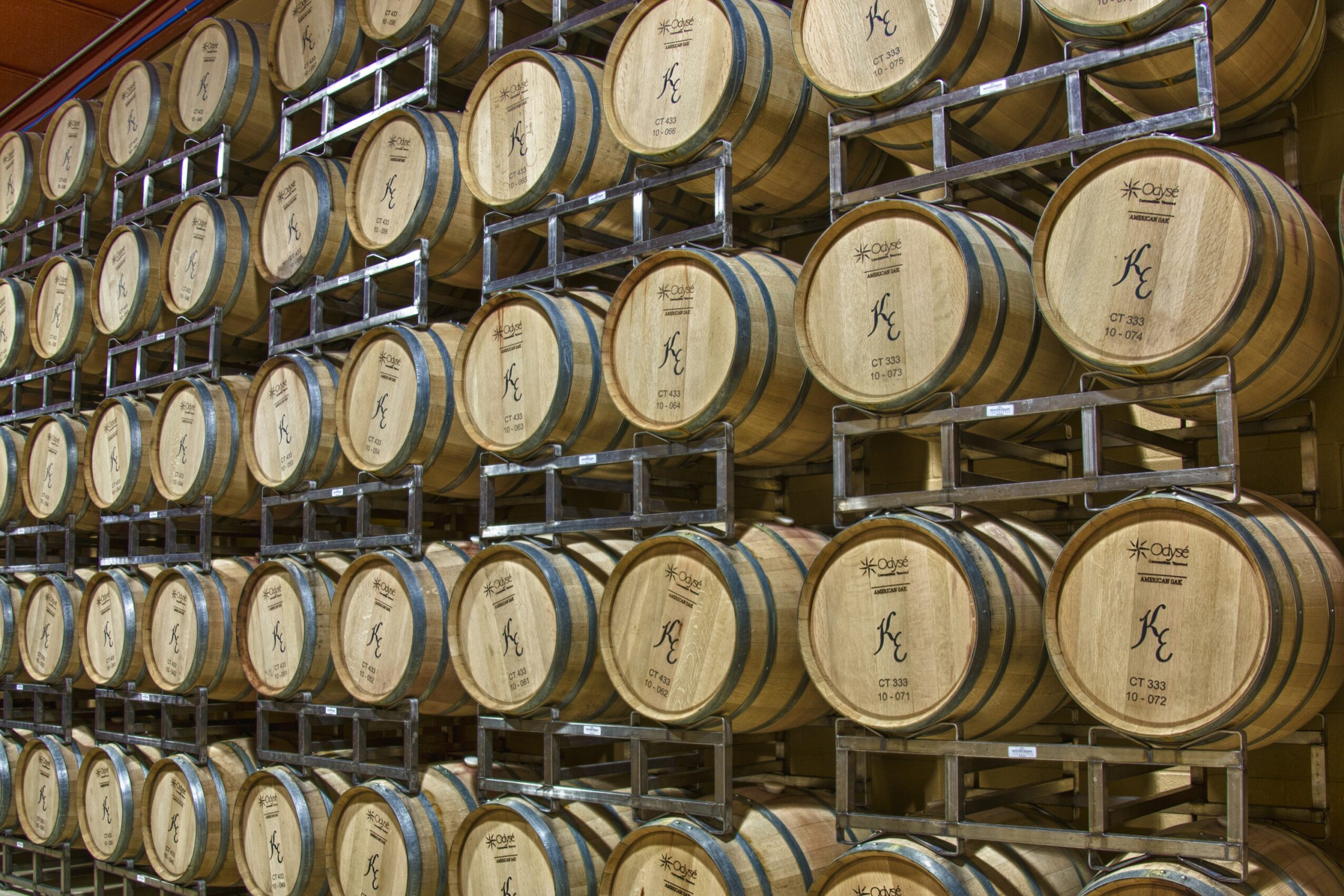 Rows of wooden barrels stored on metal racks in a cellar or storage area.