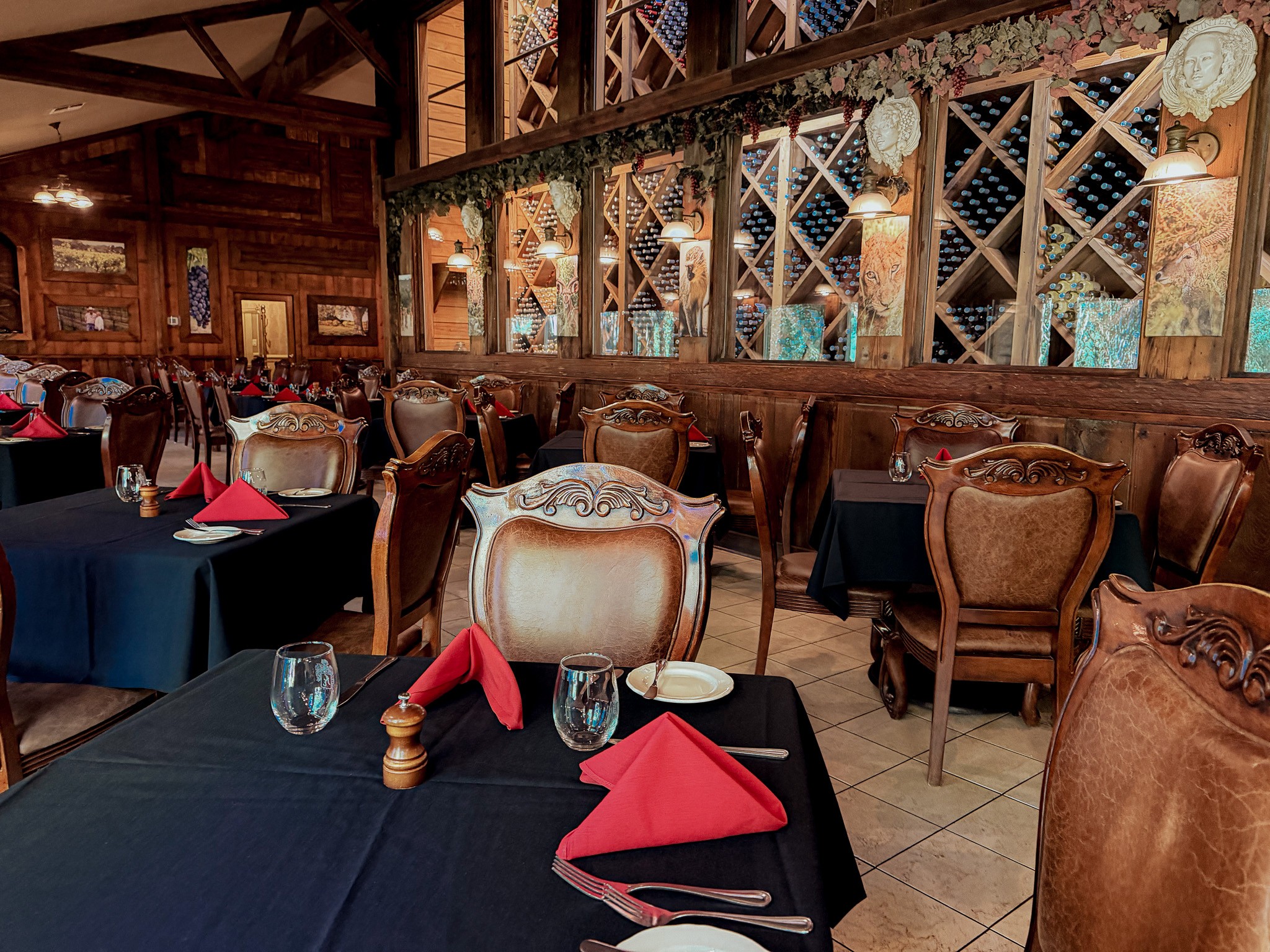 Elegant restaurant interior with wooden decor, tables with black tablecloths, red napkins, and upholstered chairs.