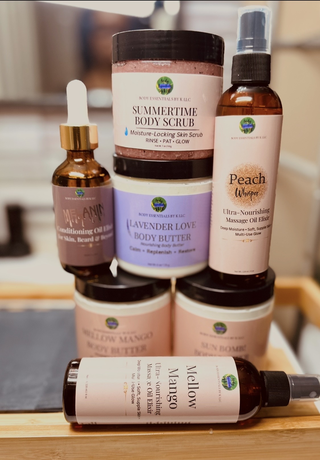 Stacked skincare products including body scrub, body butter, spray, and massage oil on a mirror surface.
