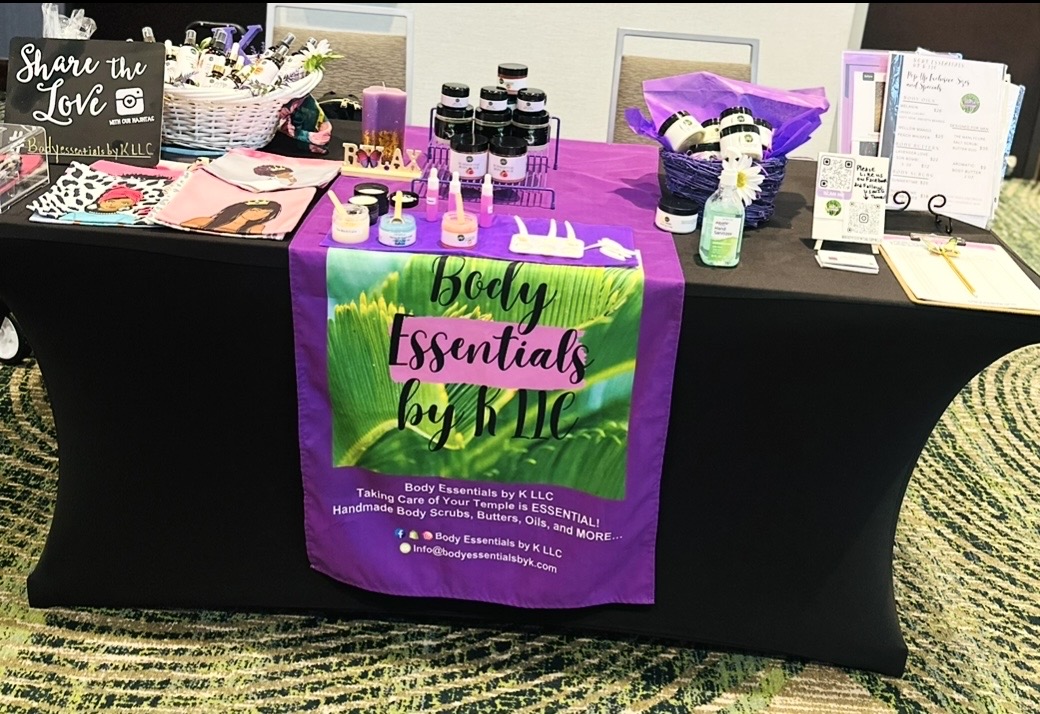 Table with body essentials products, informational materials, and a purple and green banner reading 'Body Essentials by KLL'.