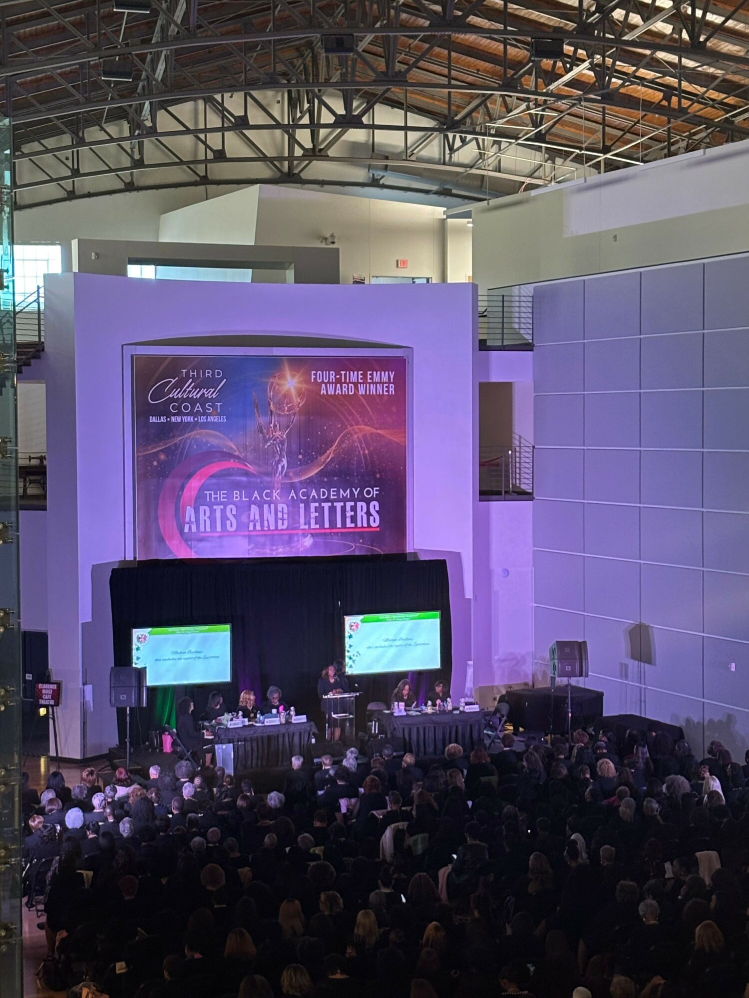Large audience watching a presentation on a stage with a screen displaying a colorful graphic and text.