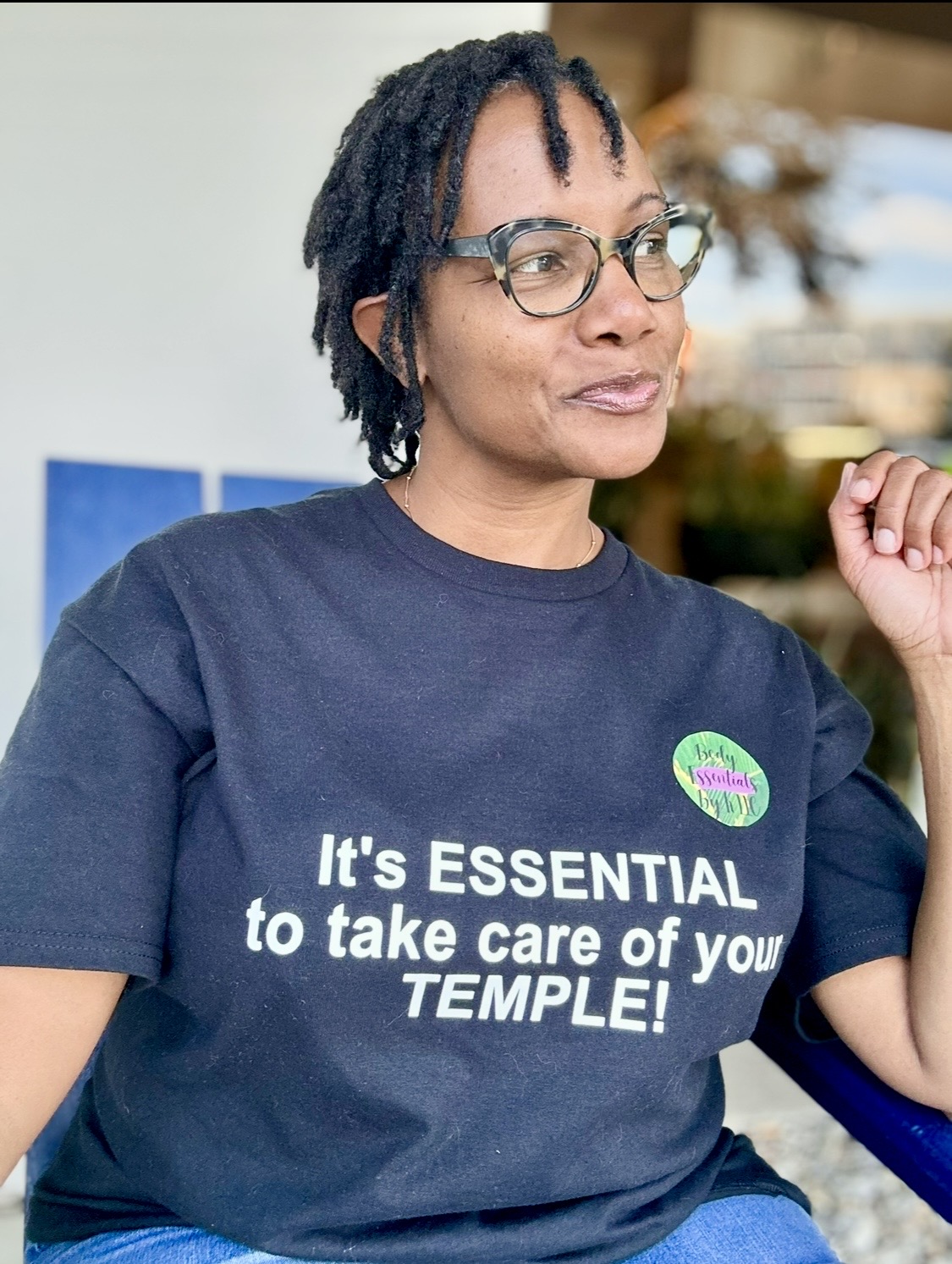 Woman with glasses wearing a navy T-shirt with text, in an indoor setting.