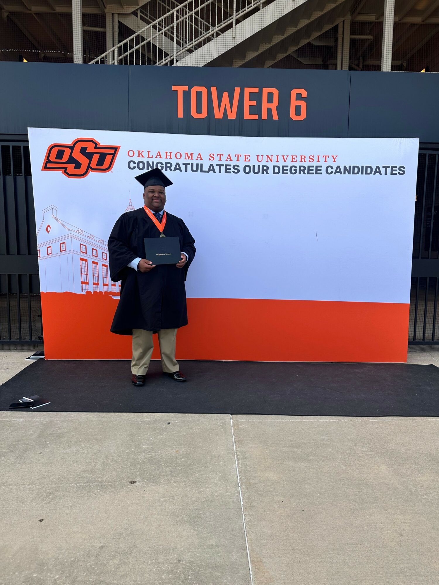 Person standing in front of a sign with OSU and Tower 6, holding a certificate, on a concrete surface.