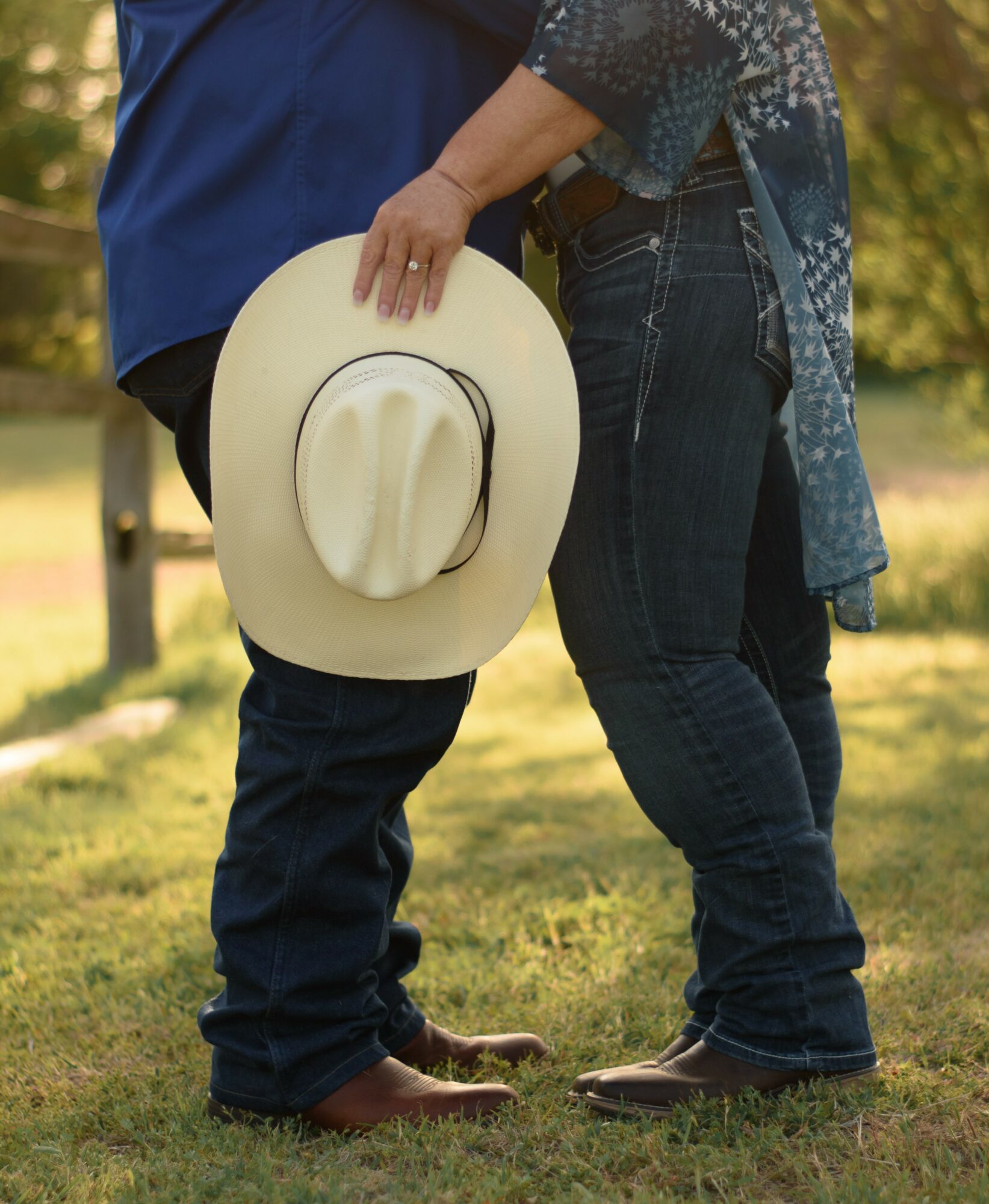 Two people standing outdoors, one holding a hat, with trees and grass in the background.