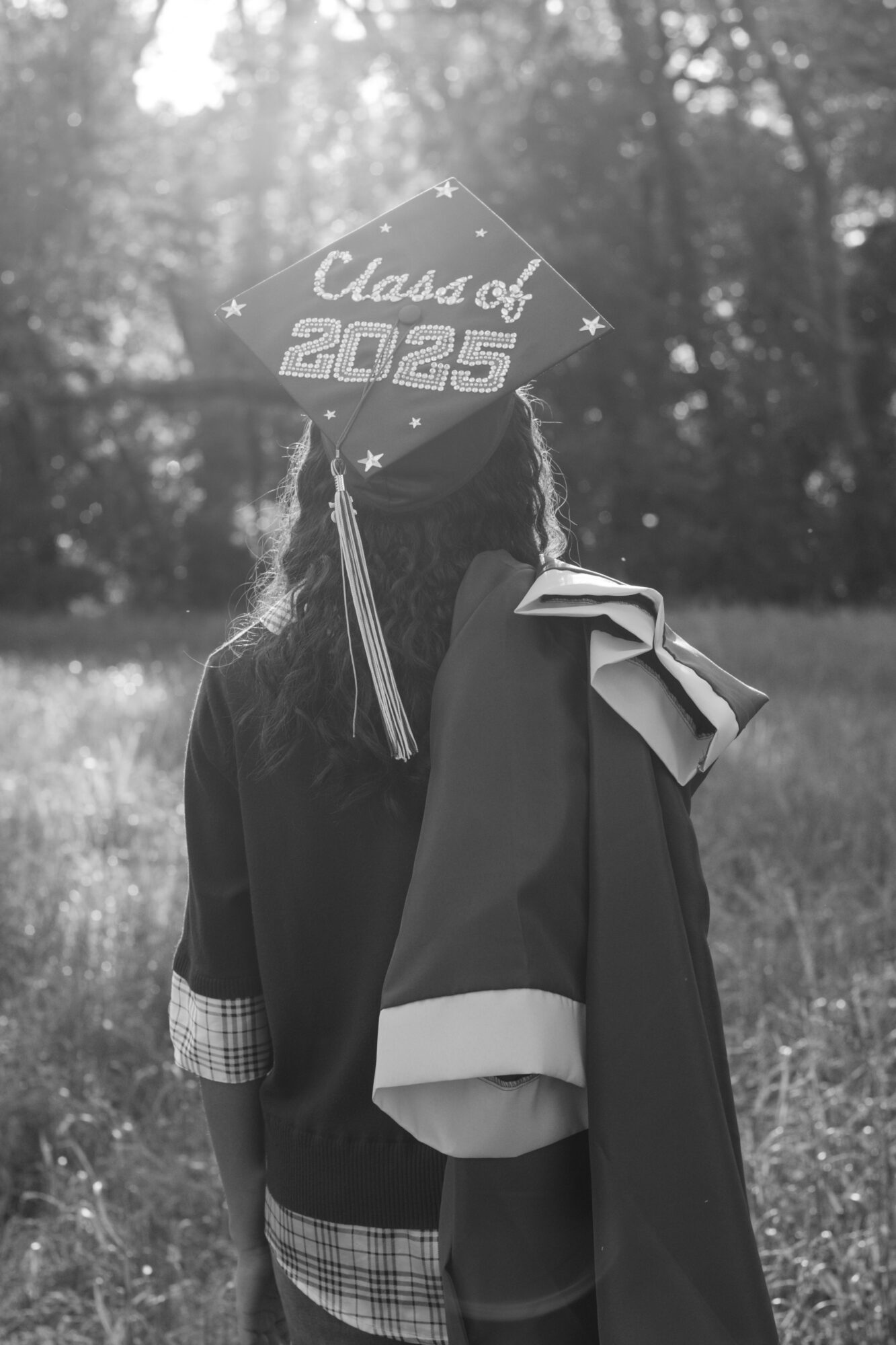 Person in graduation cap and gown outdoors, holding a diploma, with trees in background.