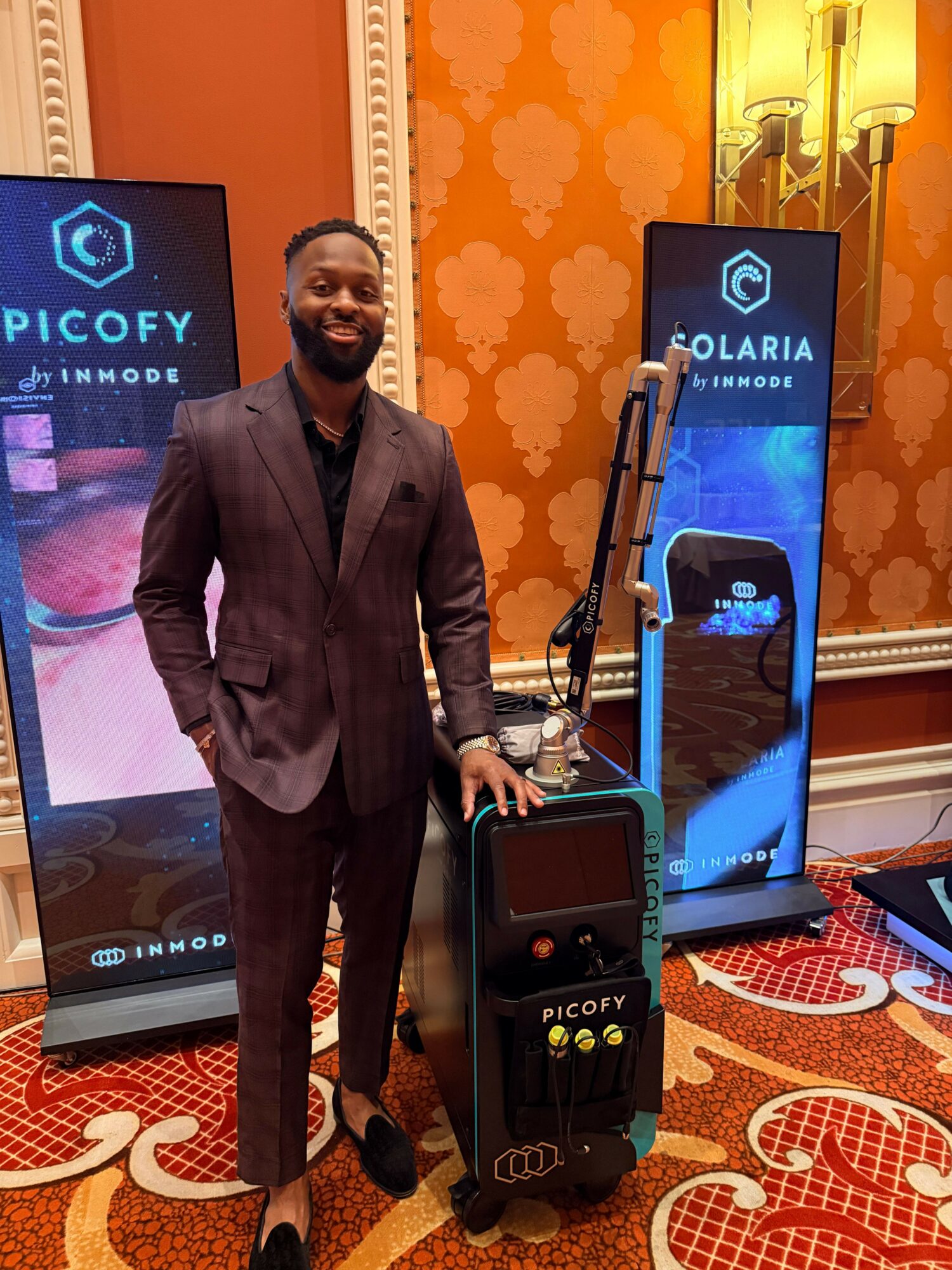 Man in suit standing next to a display with a large phone and electronic equipment, in a decorated room.