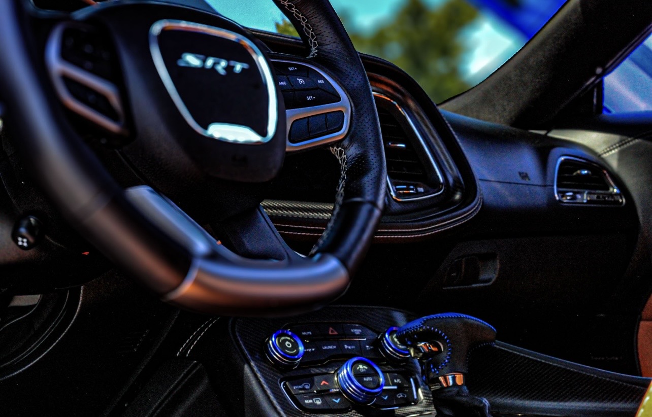 Car interior with steering wheel and dashboard controls visible, including a logo on the steering wheel.