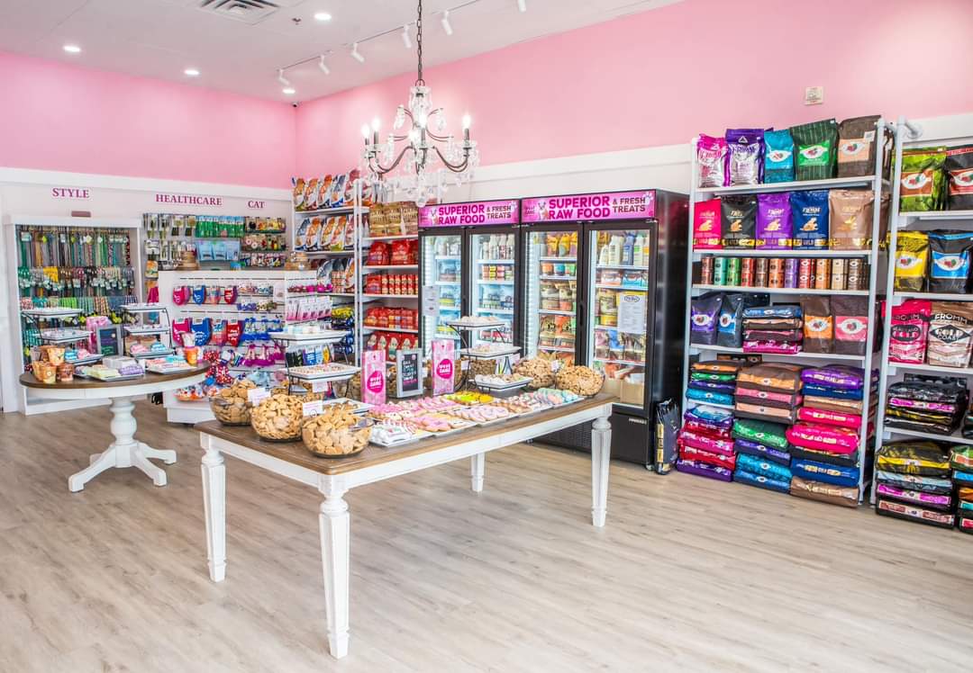 Store interior with pink walls, shelves of snacks, drinks, and school supplies, and a white table with snacks, chandelier overhead.