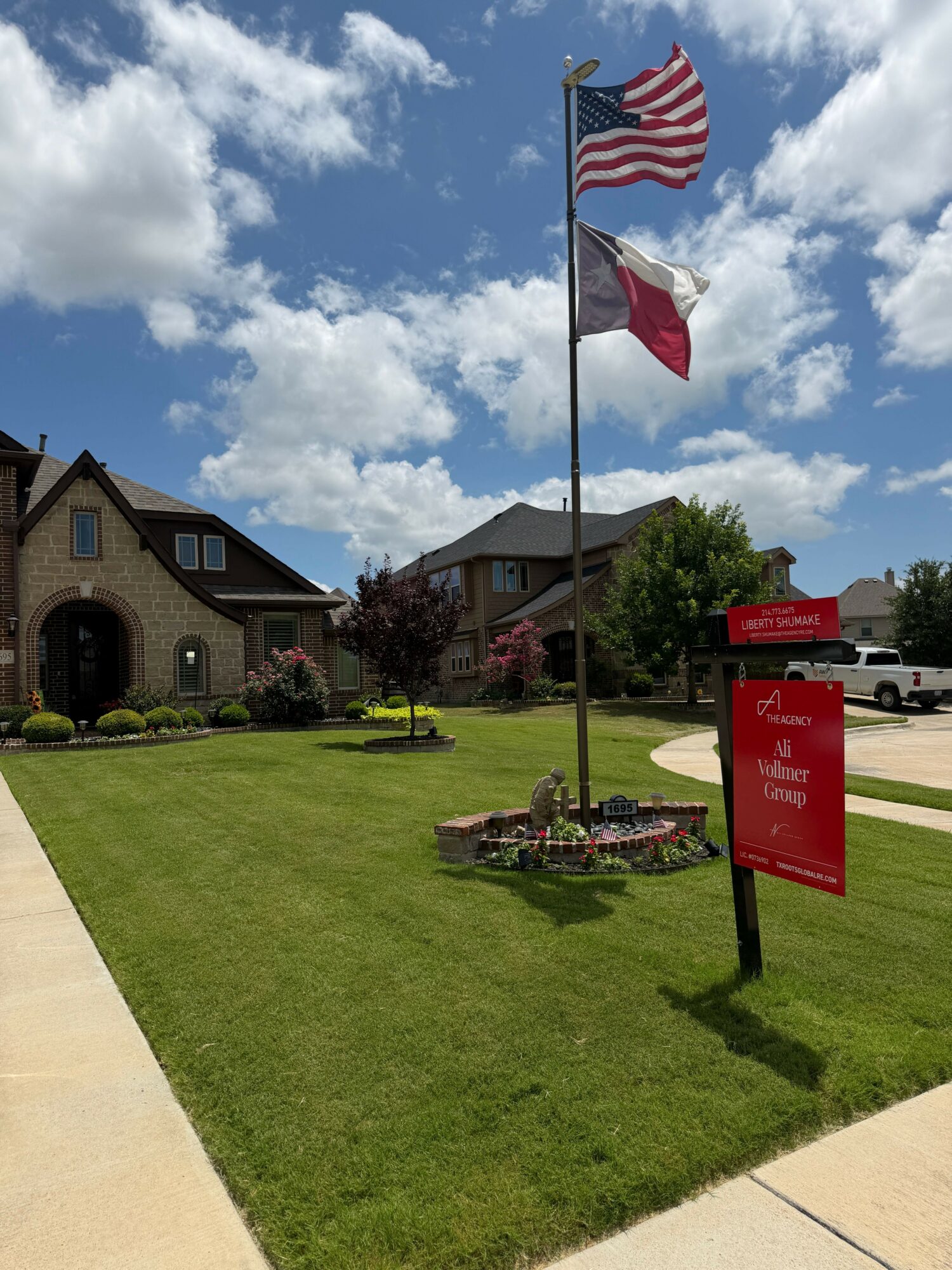 Flags on flagpoles in front of a building with a lawn and sidewalk, under a partly cloudy sky.