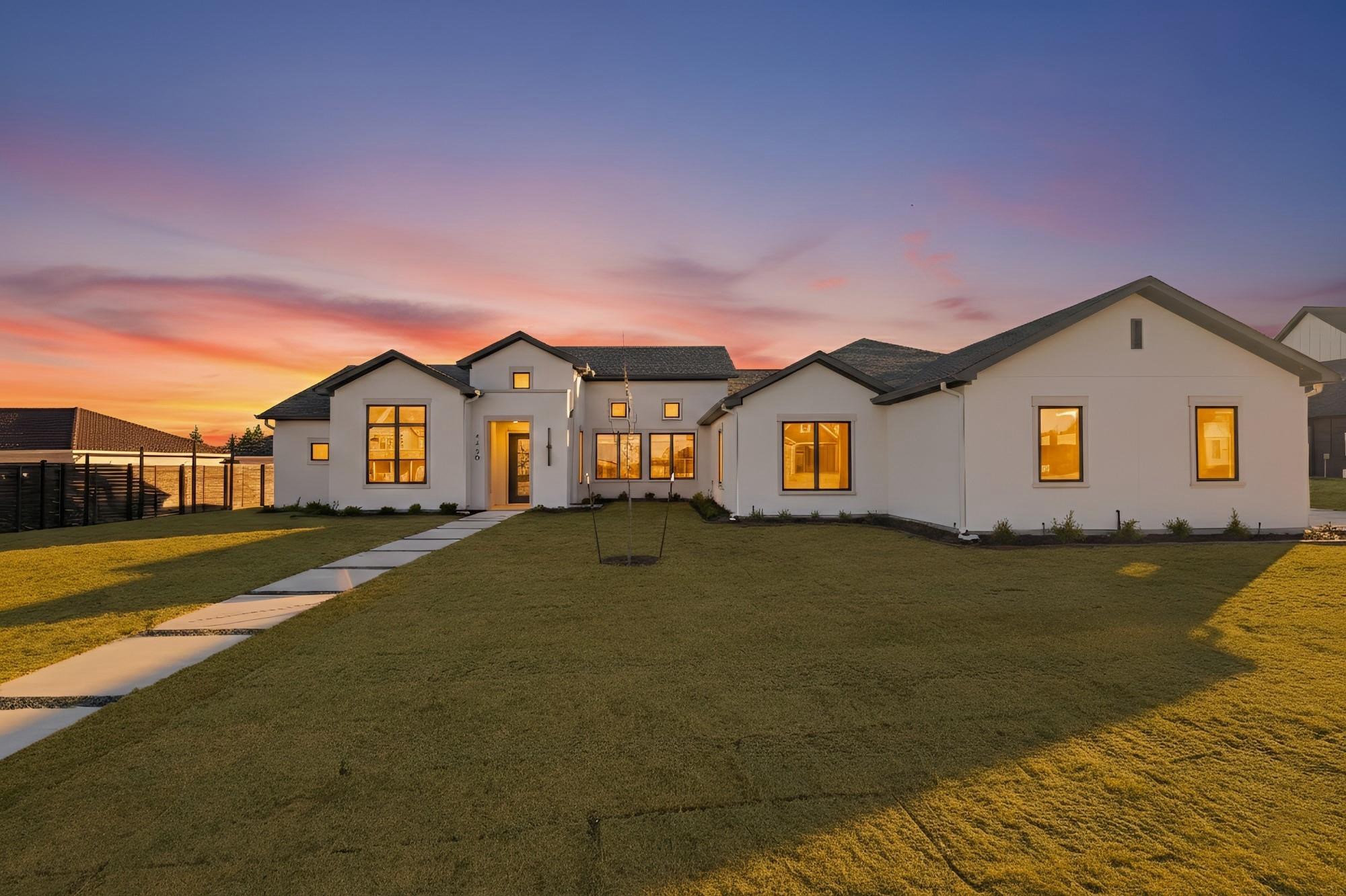 White house with multiple windows and a front yard during sunset, sky with pink and purple hues.