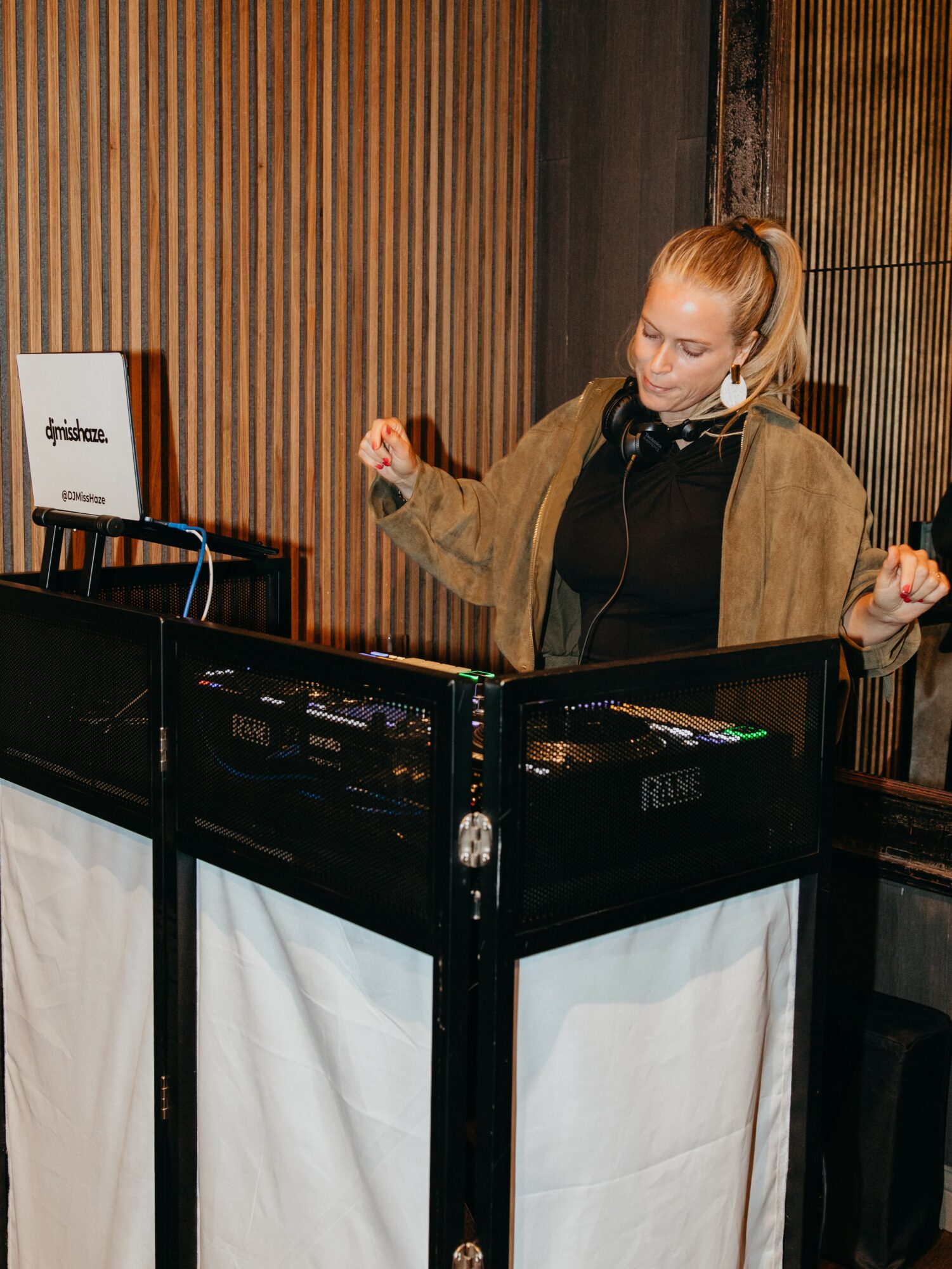 Woman DJ with headphones at turntables in a wooden-paneled room, focused on mixing music.
