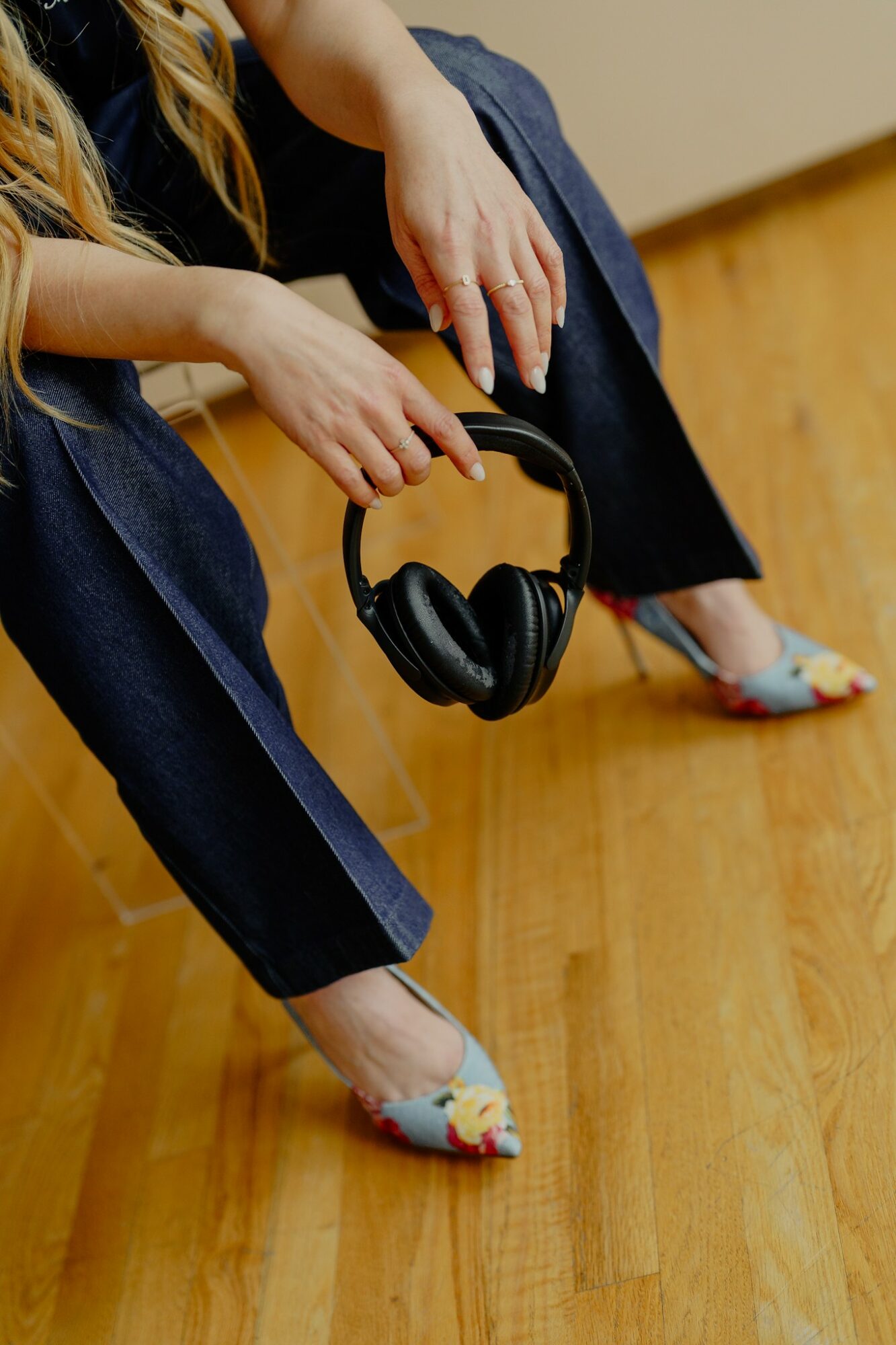 Person sitting on a wooden floor holding headphones, with legs crossed and wearing colorful shoes.