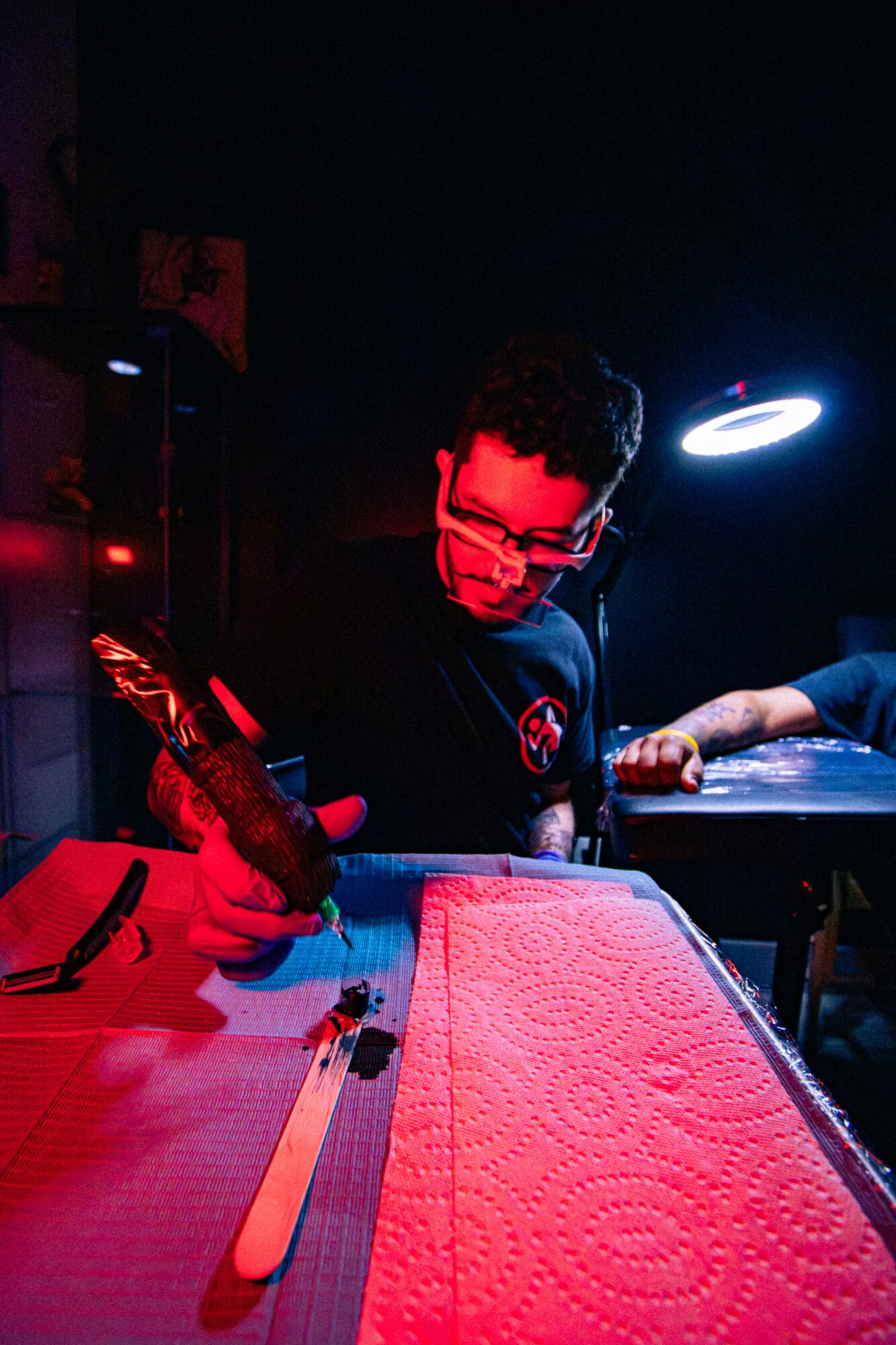 Person with glasses writing on a surface under a bright light, with a dark background and red and blue lighting.