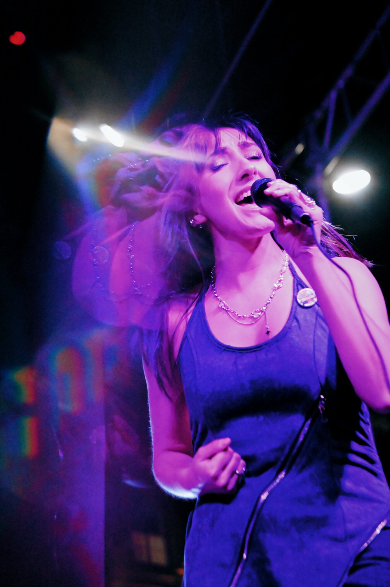 Female singer performing passionately on stage with microphone, purple lighting, and dark background.