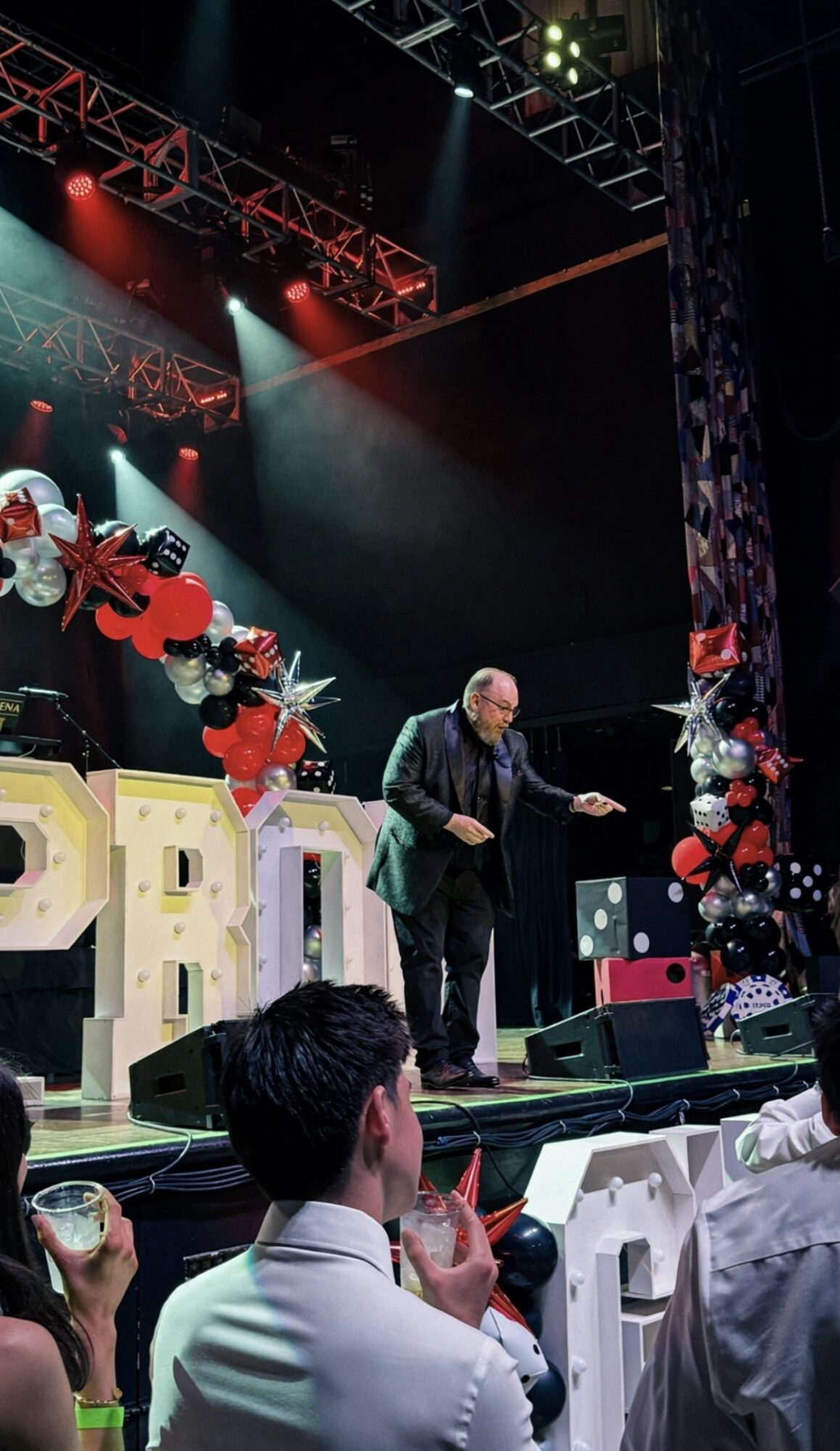 Speaker on stage with decorations, audience seated, colorful lighting, and large letters spelling 'PRO' in the background.